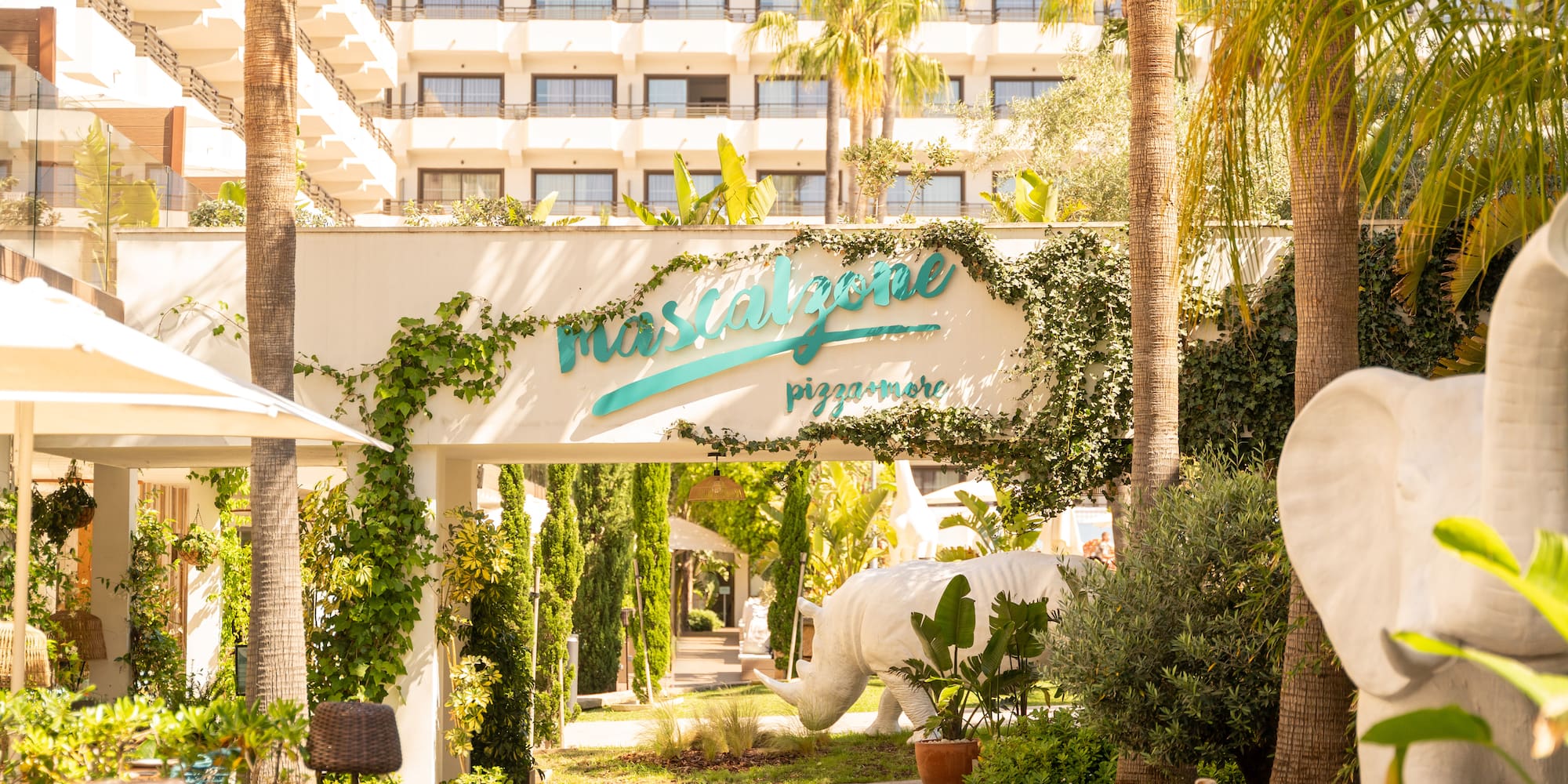 Mascalzone pizzamore entrance with palm trees, rhino, elephant statues, resort hotel.