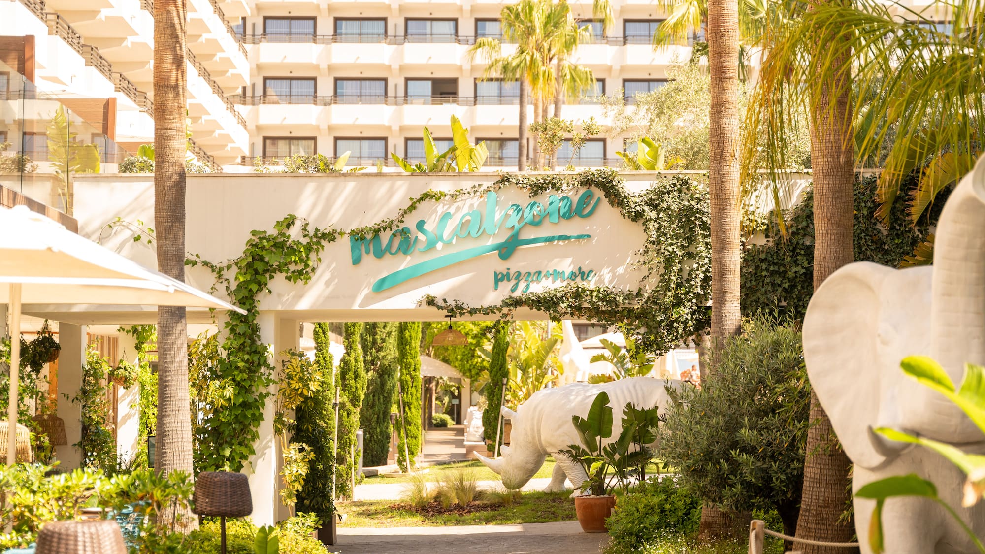 Mascalzone pizzamore entrance with palm trees, rhino, elephant statues, resort hotel.