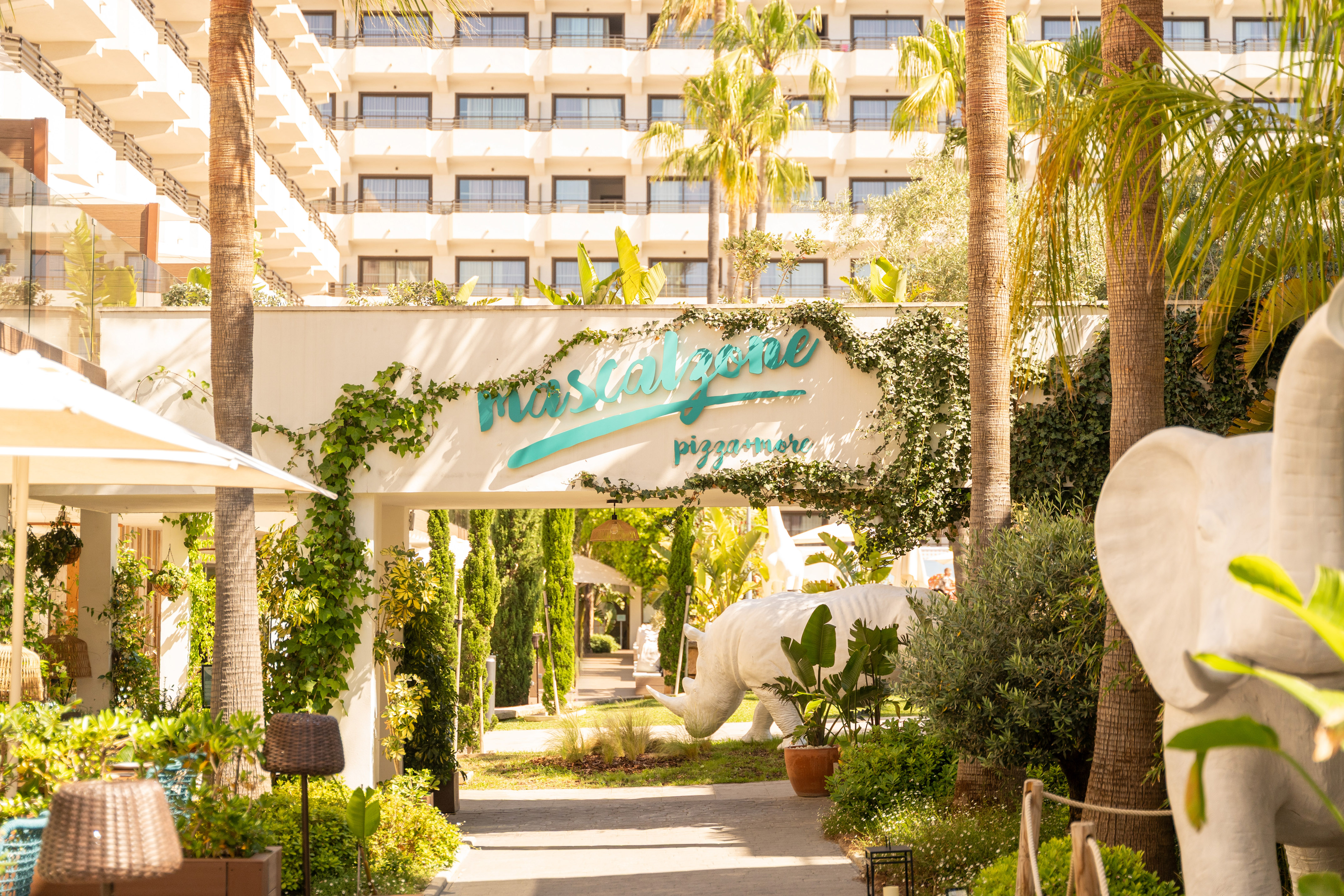 Mascalzone pizzamore entrance, tropical palms, ivy arch, white rhino statue.