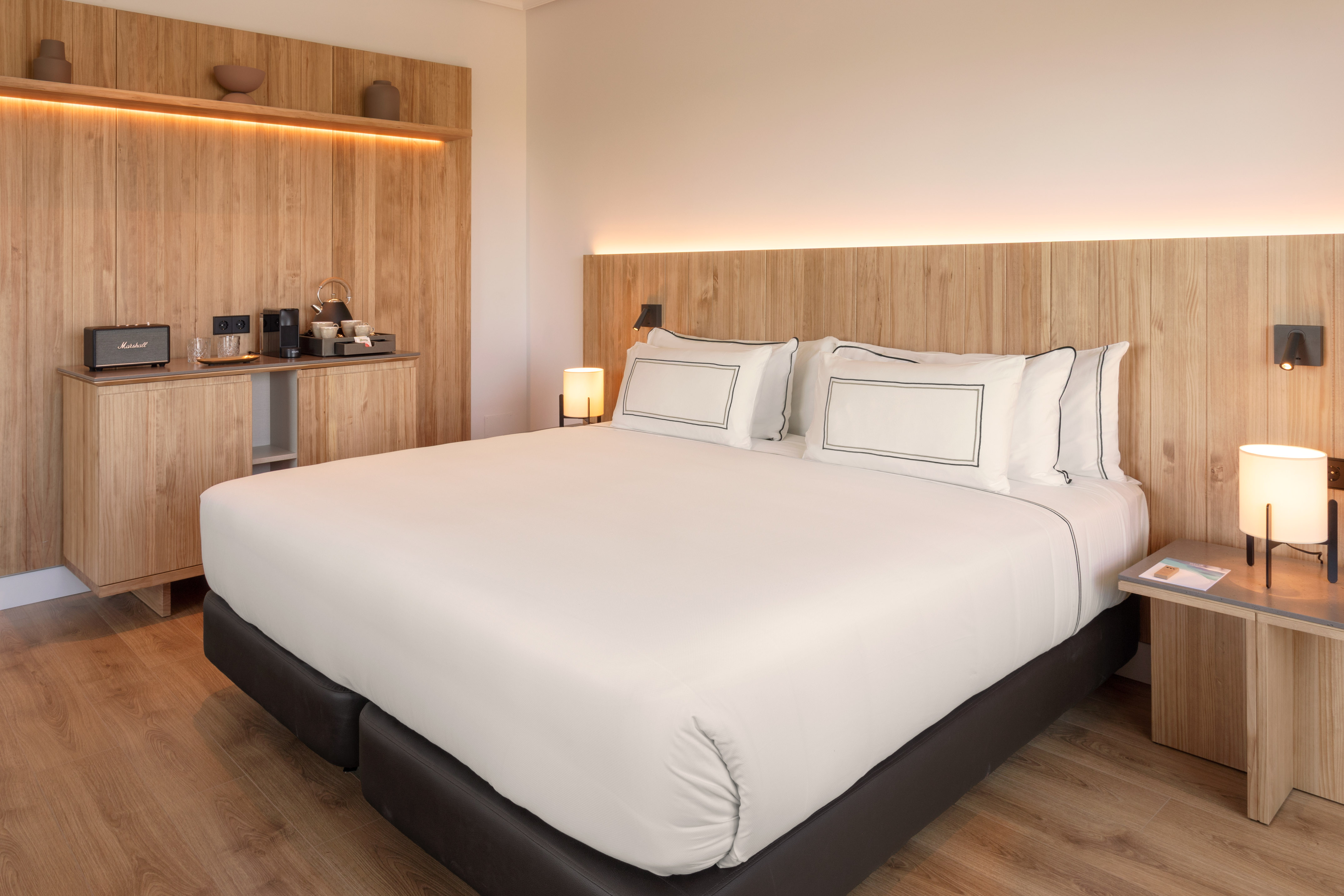 Hotel bedroom with wooden headboard, large bed, ambient lighting, and coffee station.
