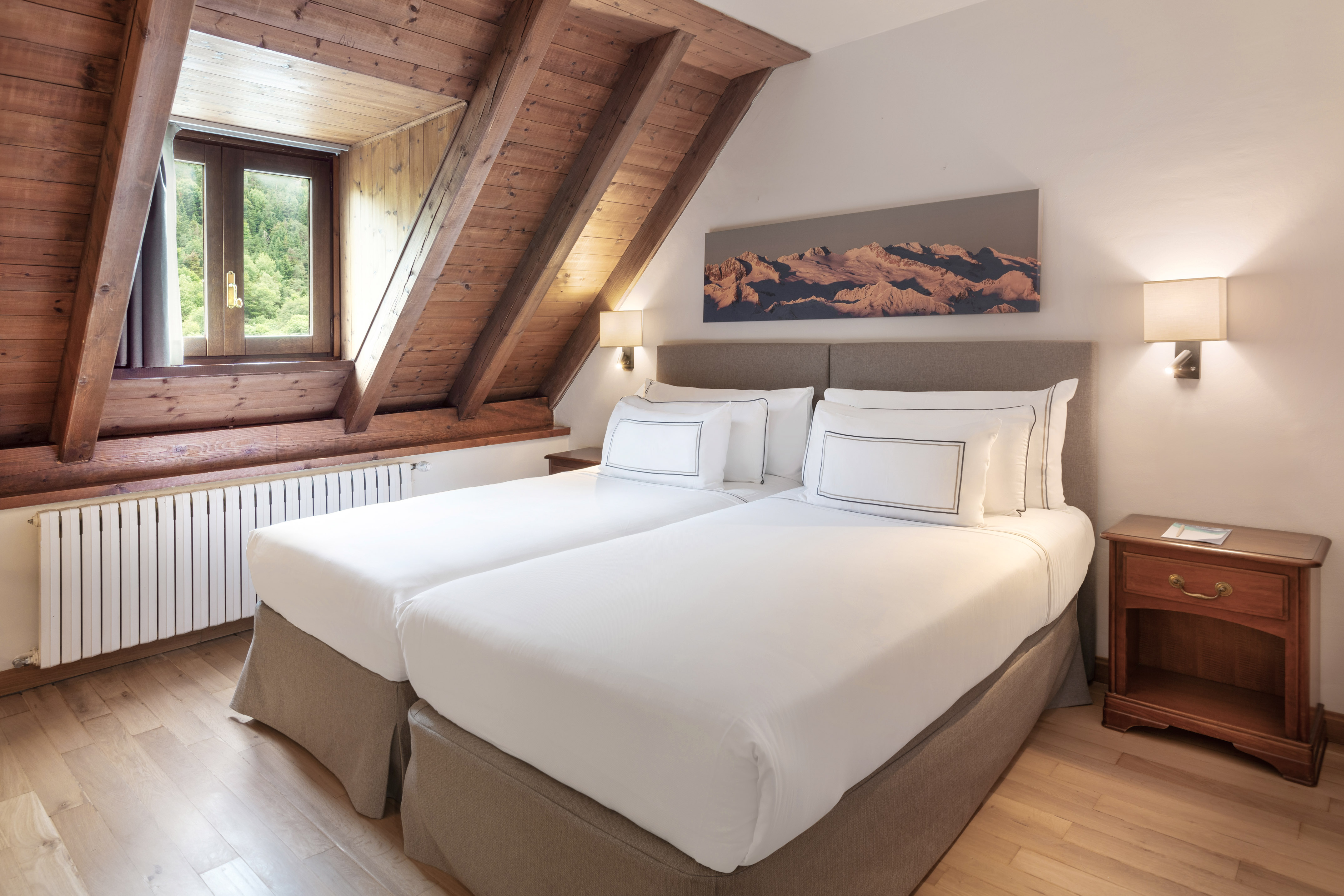 Twin beds in an attic hotel room with wooden ceiling and mountain view.