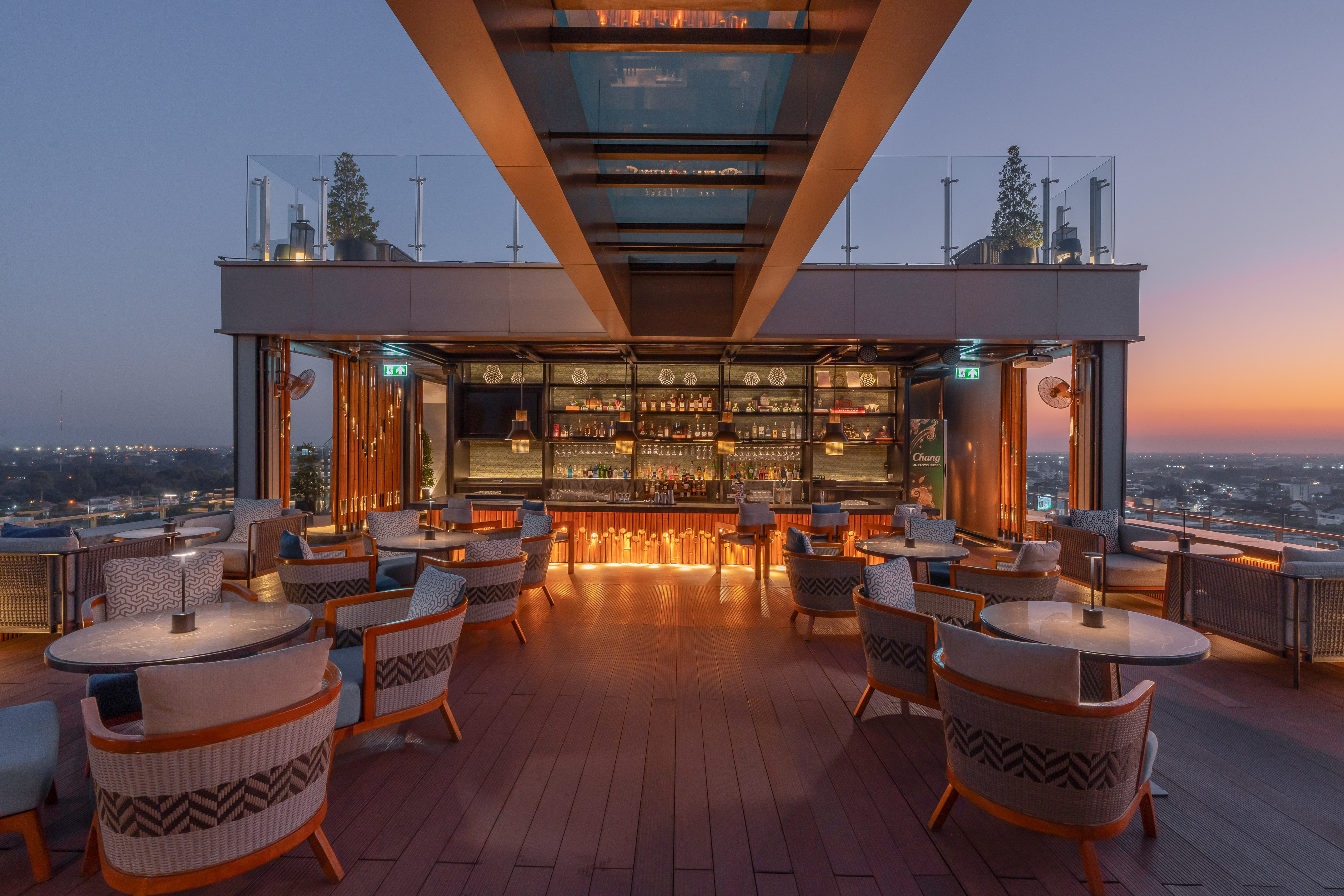 Terraza-bar iluminada en azotea con vista urbana al atardecer.