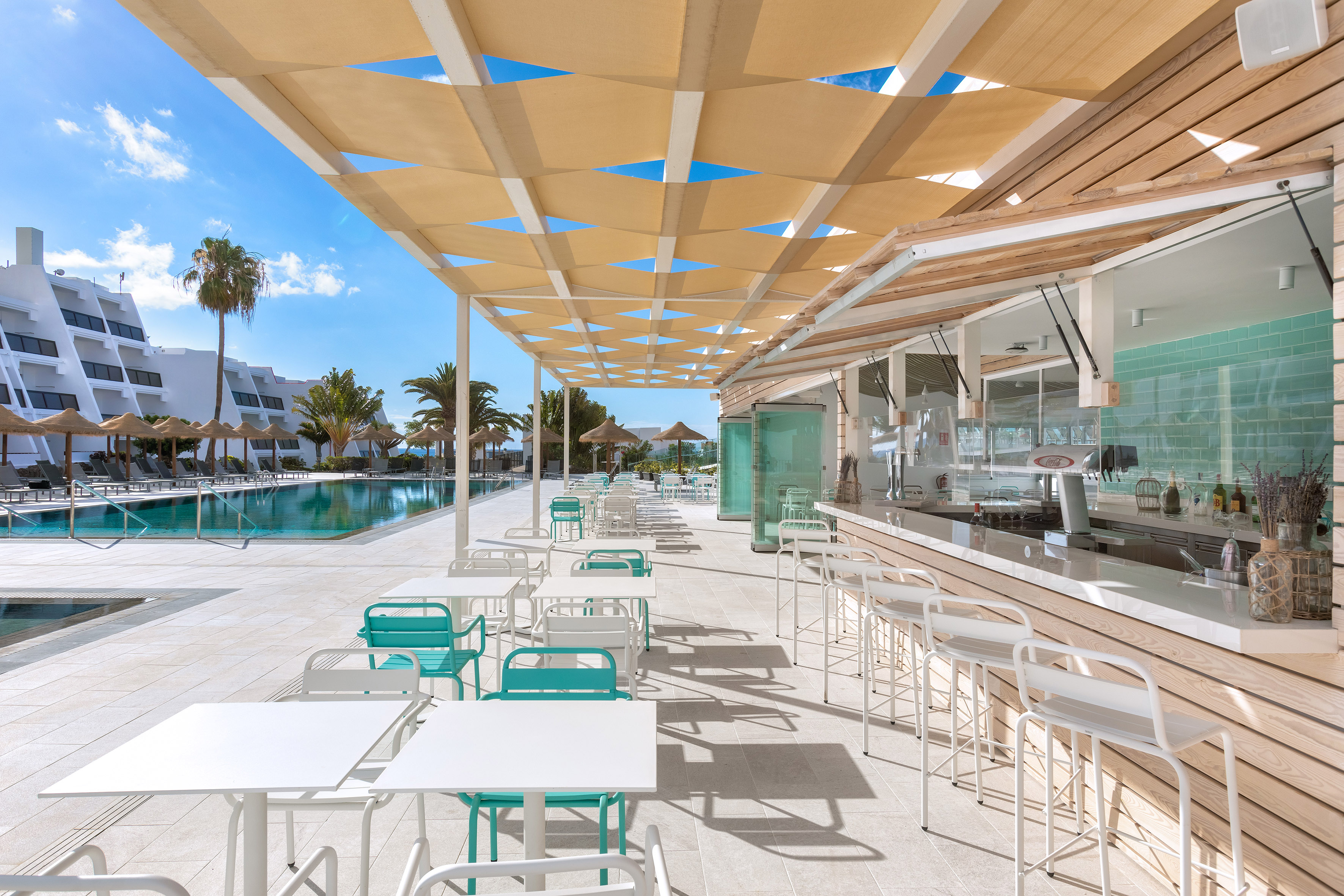 Modern resort poolside bar, outdoor dining with white and teal chairs.