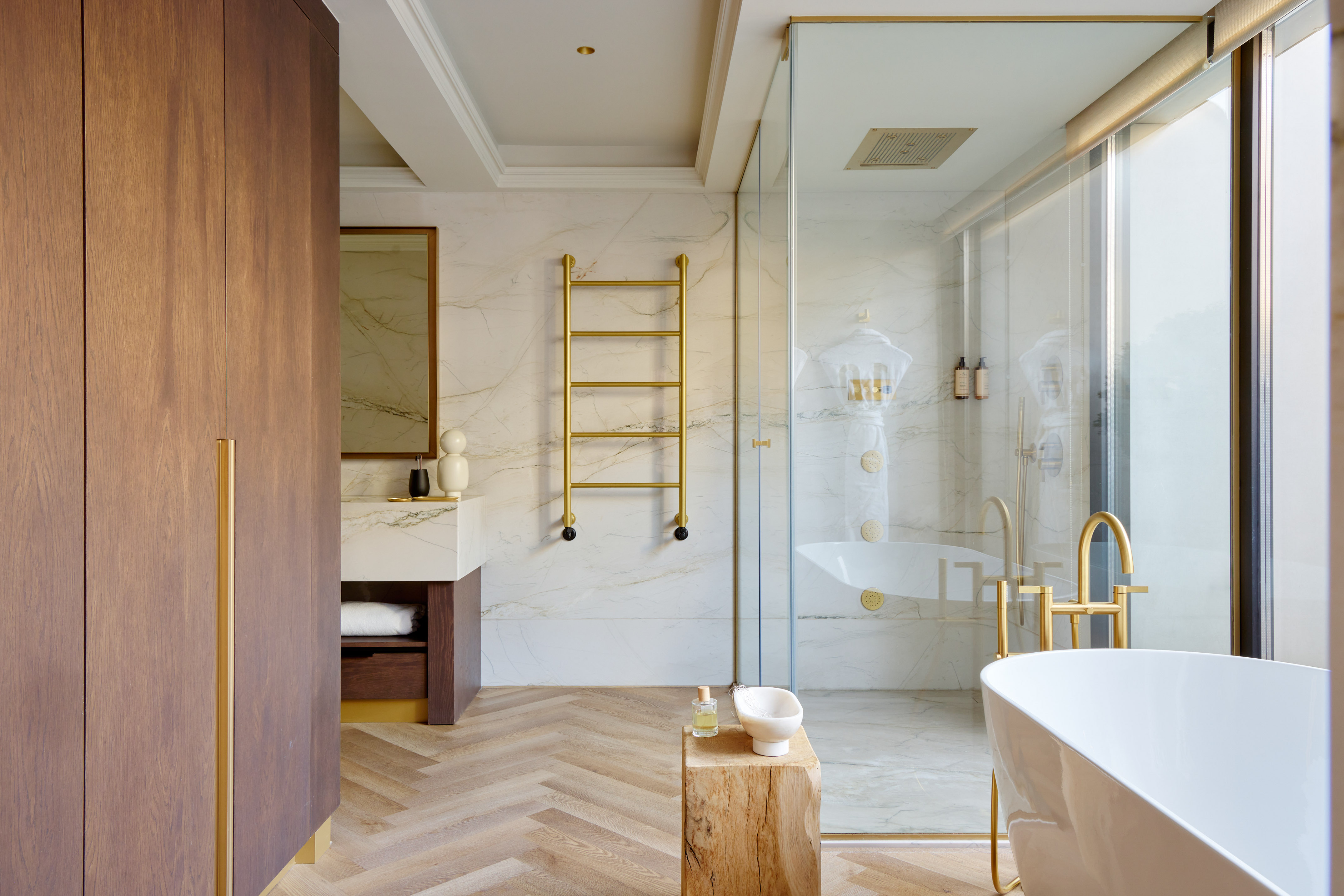 Modern bathroom with marble, gold fixtures, wood floor, freestanding tub, and shower.