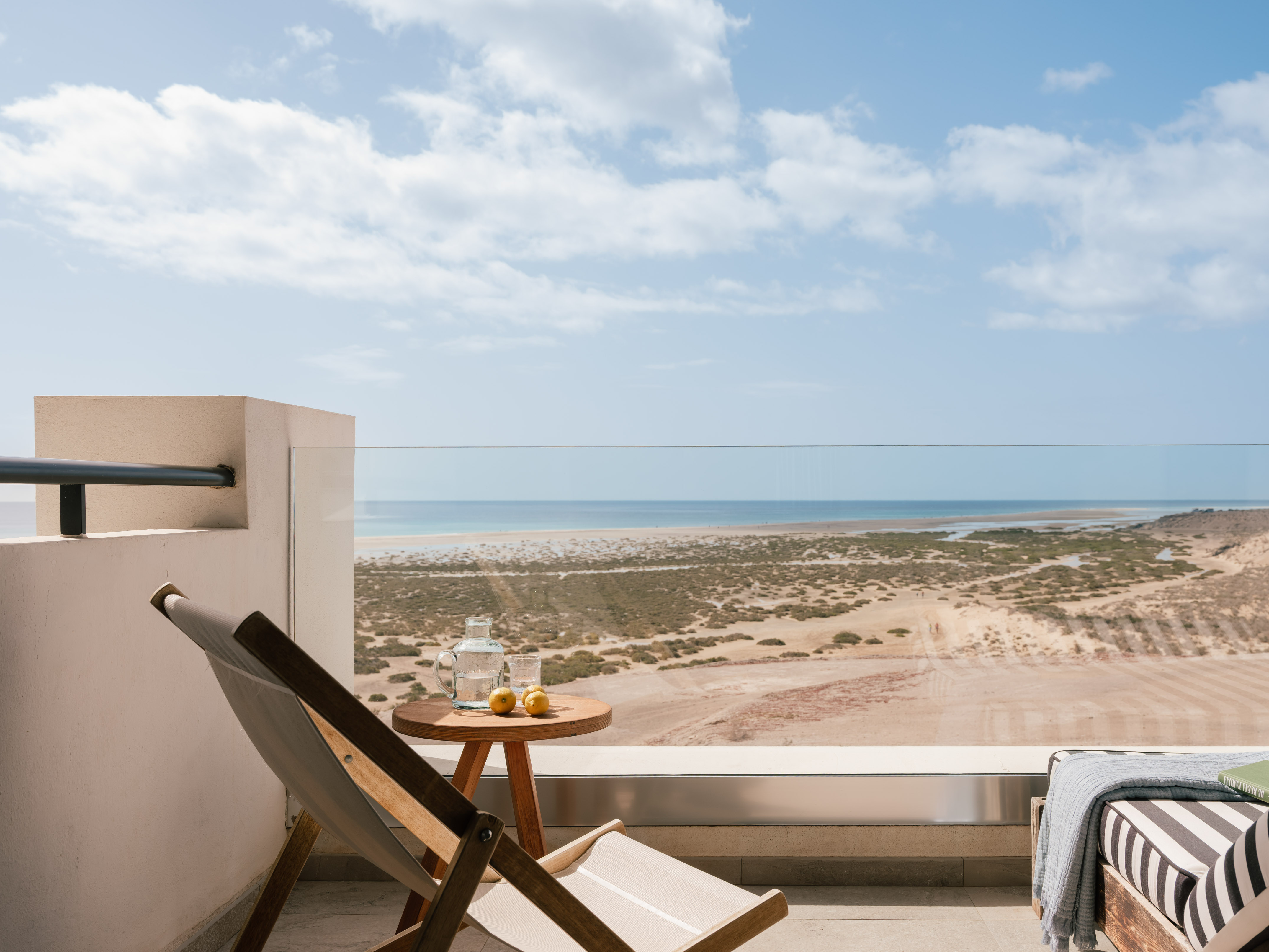 Balcony with ocean view, lounge chair, table, and arid coastal landscape.