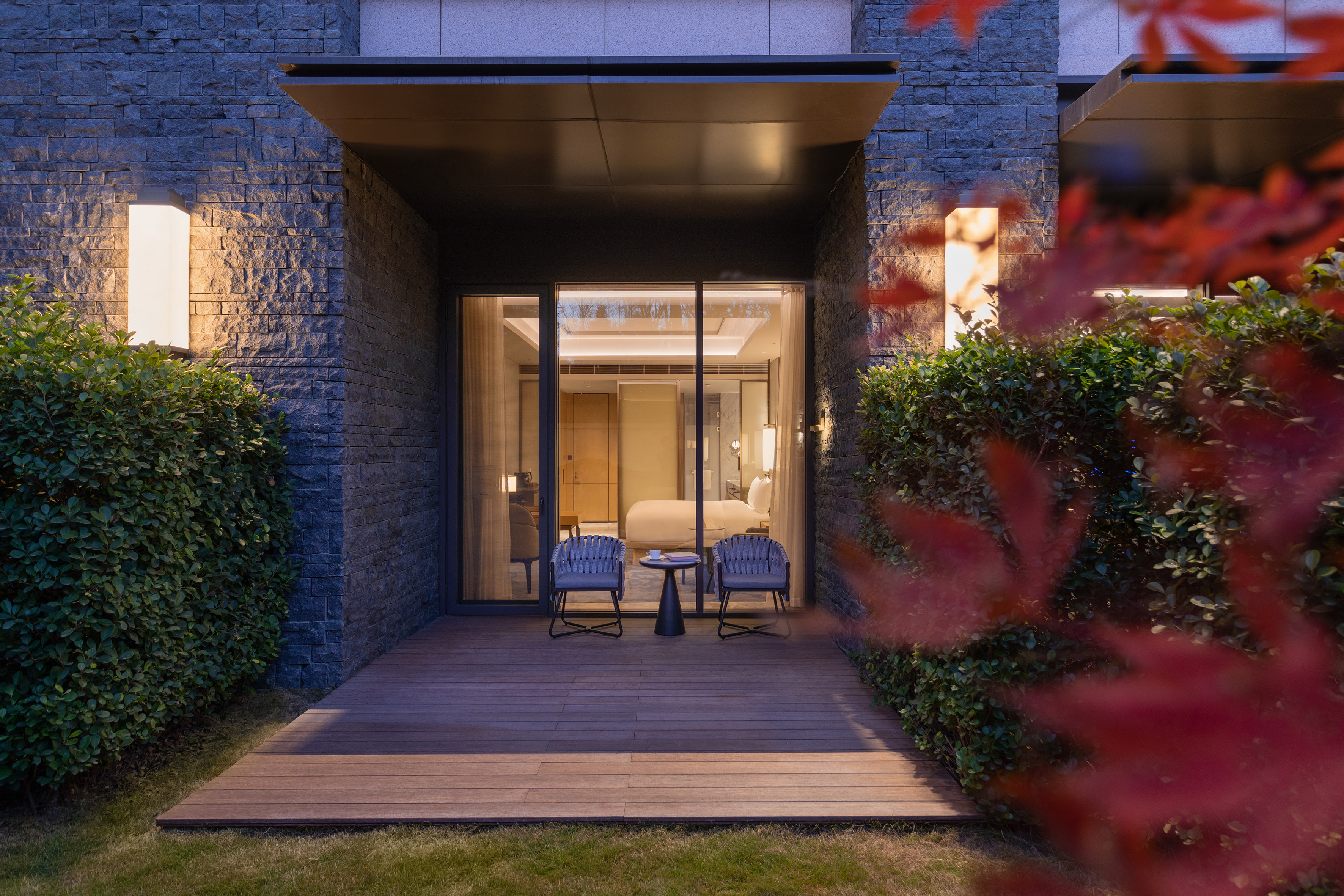 Modern hotel patio with outdoor seating, stone facade, and lush hedges.