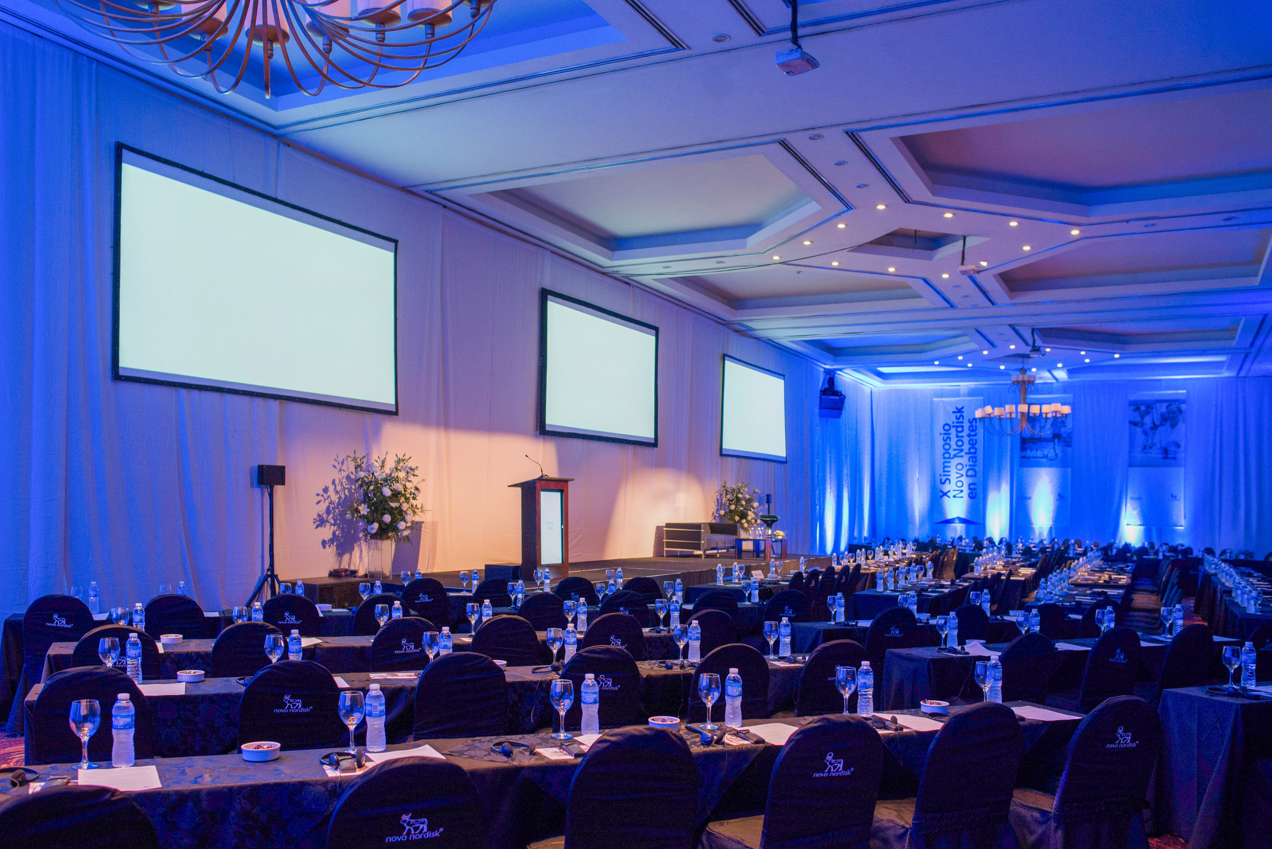 Novo Nordisk symposium conference room with screens, podium, blue lighting.