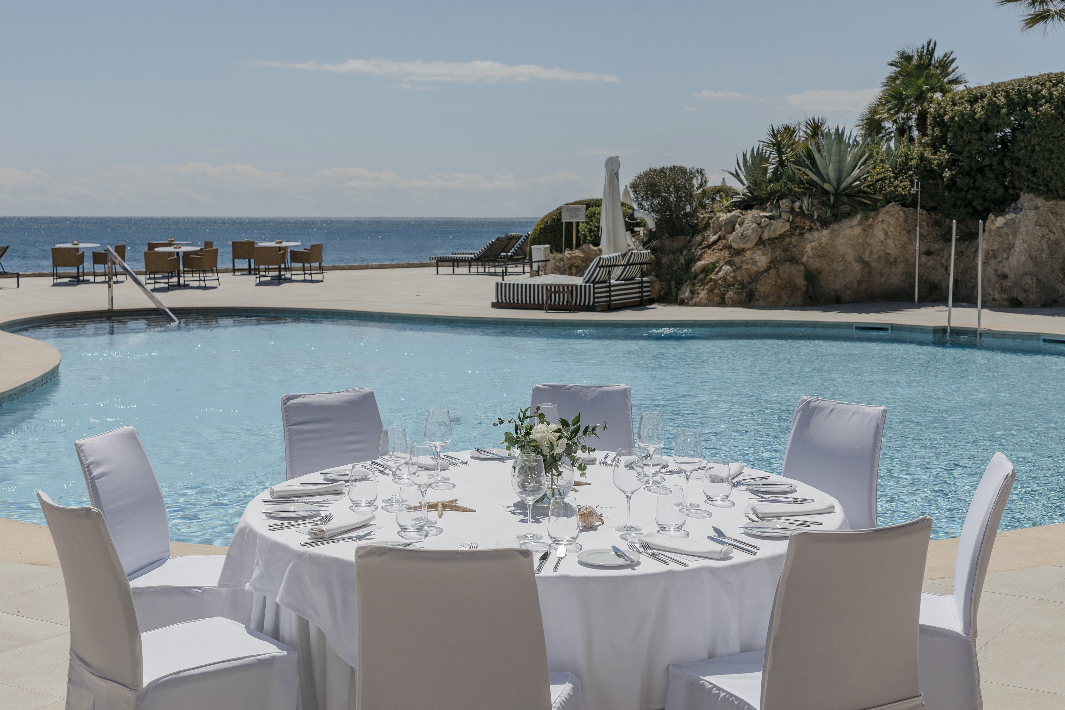 Elegant outdoor dining table by a resort pool with sparkling ocean view.