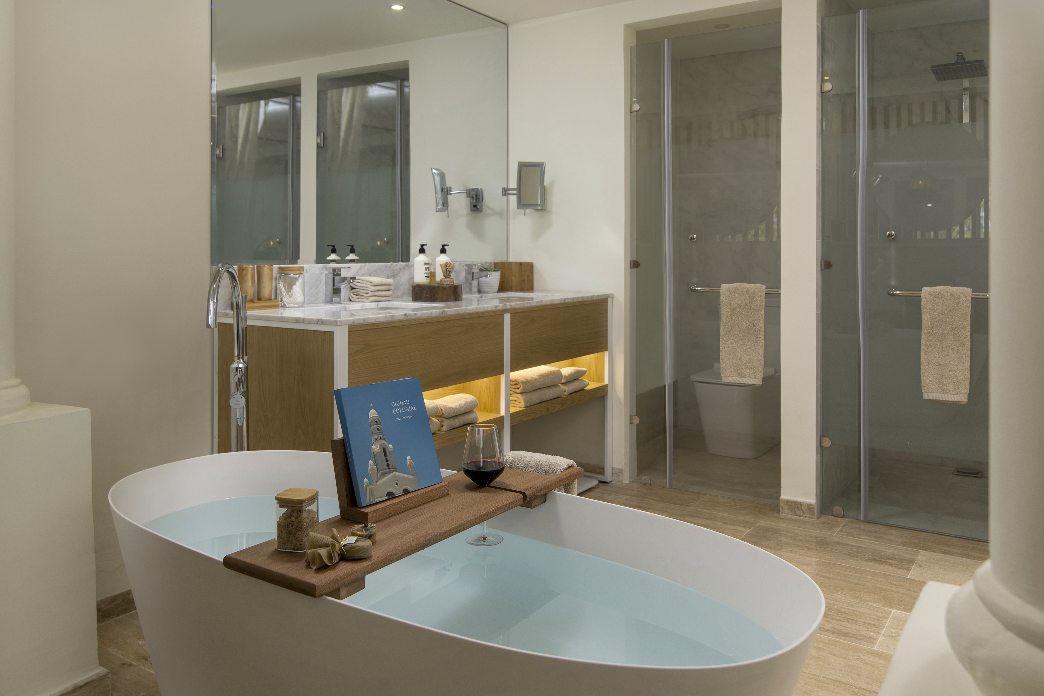 Modern hotel bathroom with freestanding tub, bath caddy, wine, and double vanity.