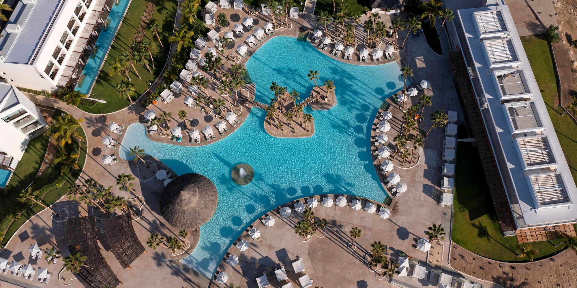 Luxury resort aerial: sprawling pool with islands, palm trees, cabanas.