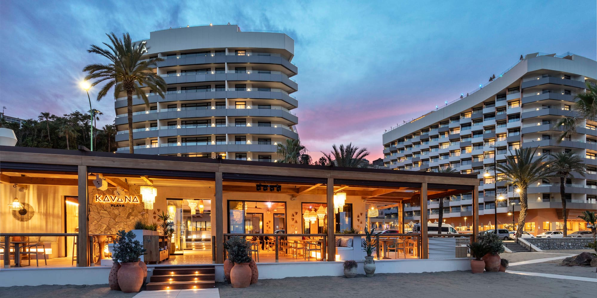 Beachfront Kavana Playa restaurant, modern resort hotels, palm trees at twilight.