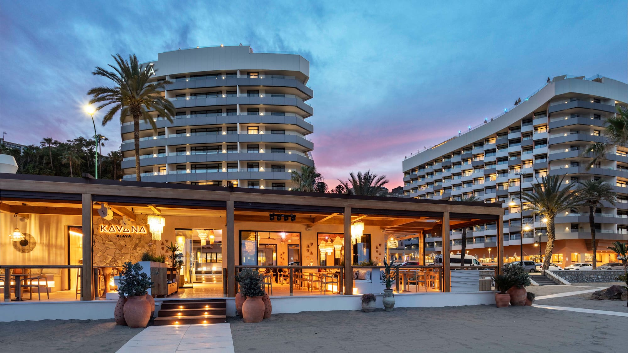 Beachfront Kavana Playa restaurant, modern resort hotels, palm trees at twilight.