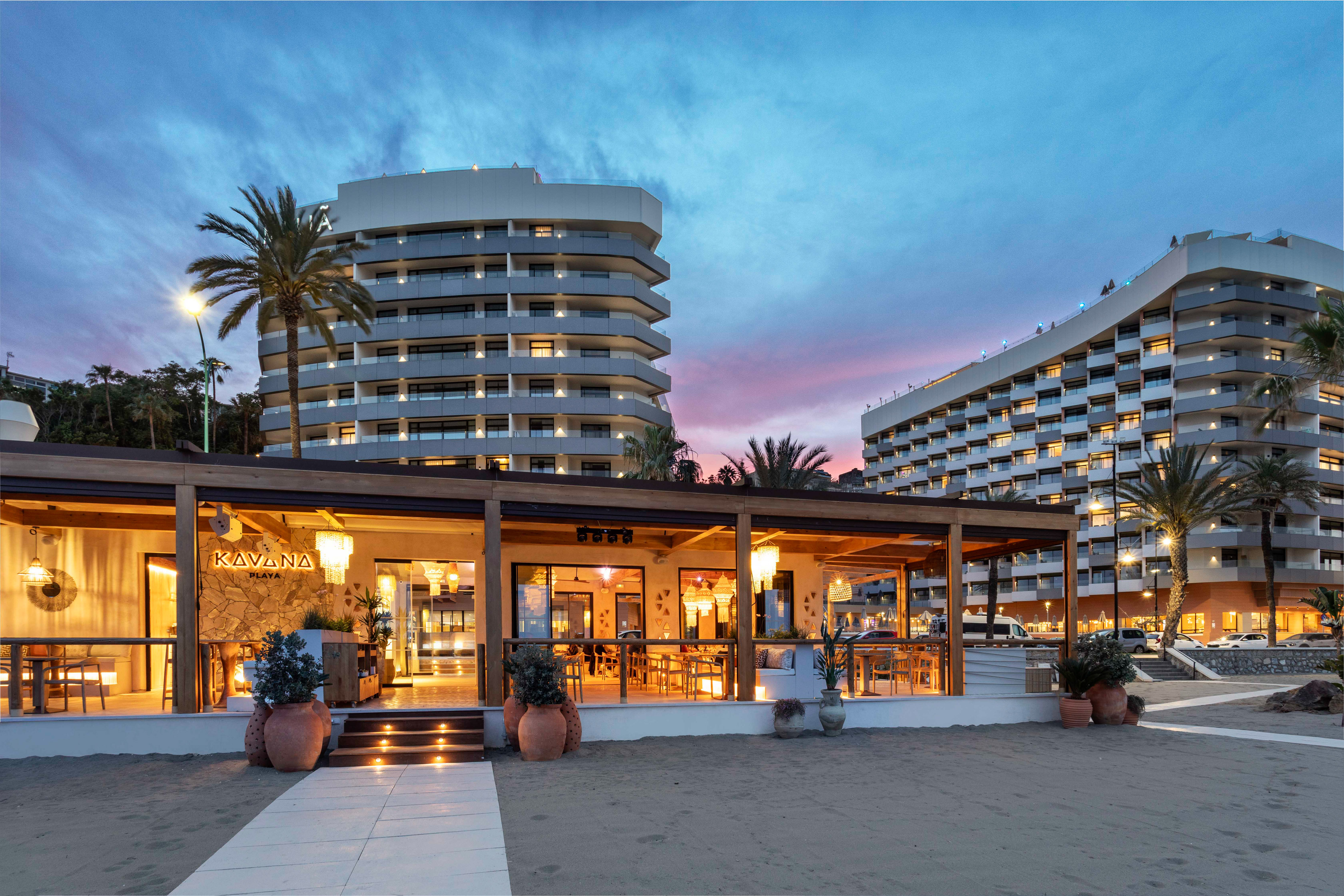 Beachfront Kavana Playa restaurant, modern resort hotels, palm trees at twilight.