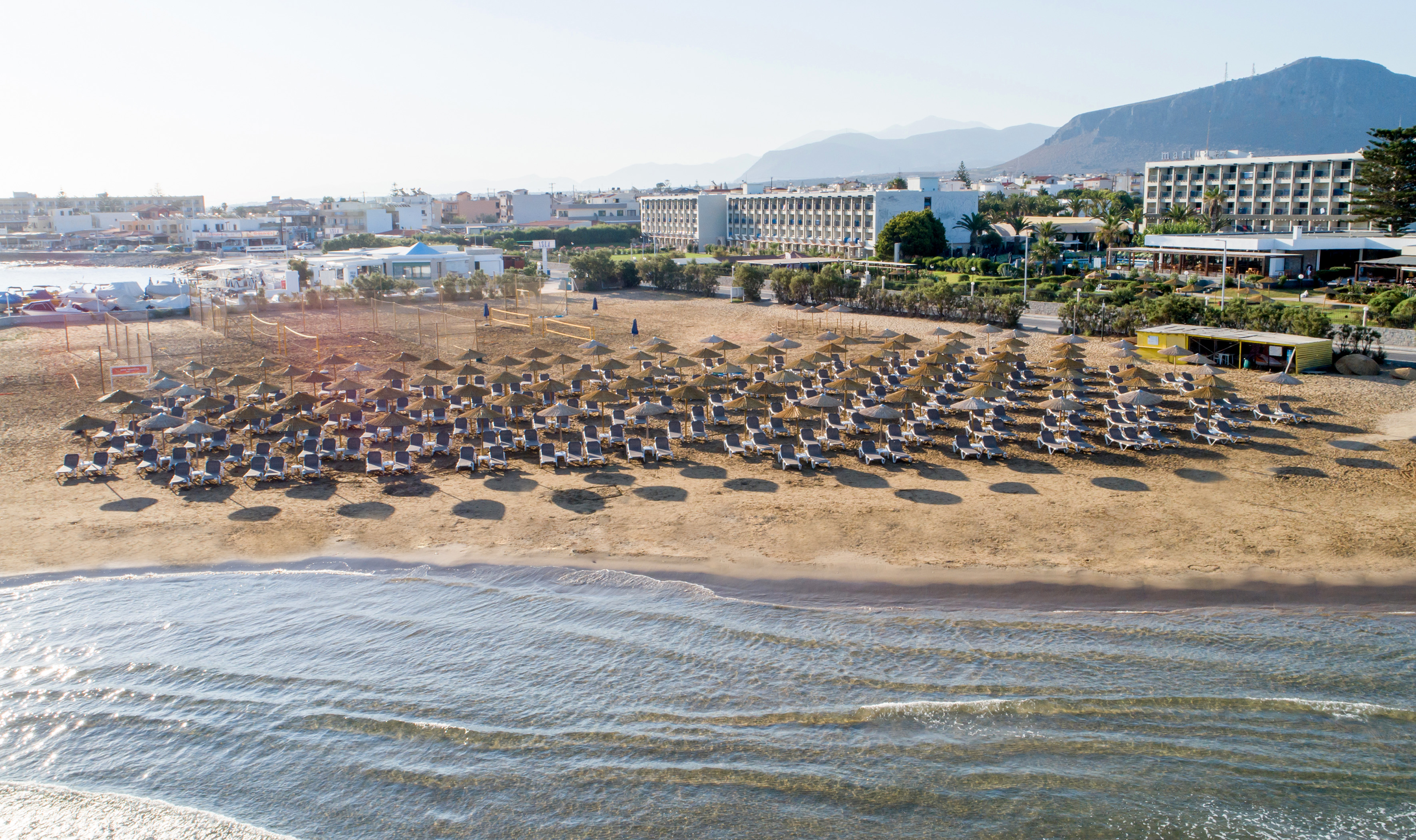 Beach resort with rows of sun loungers, straw umbrellas, and calm sea.