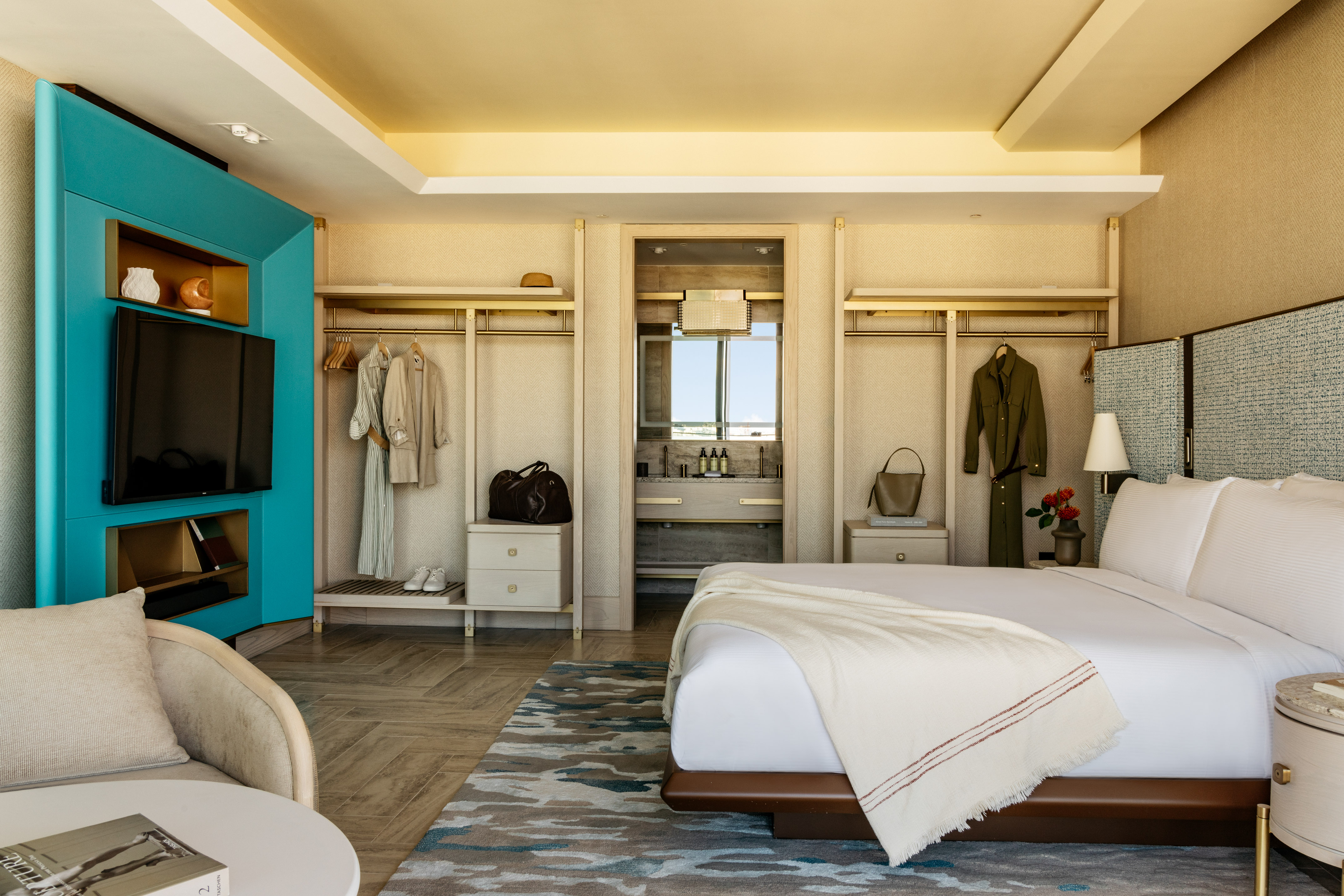Luxurious hotel bedroom with king bed, open closet, TV, and en-suite bathroom view.