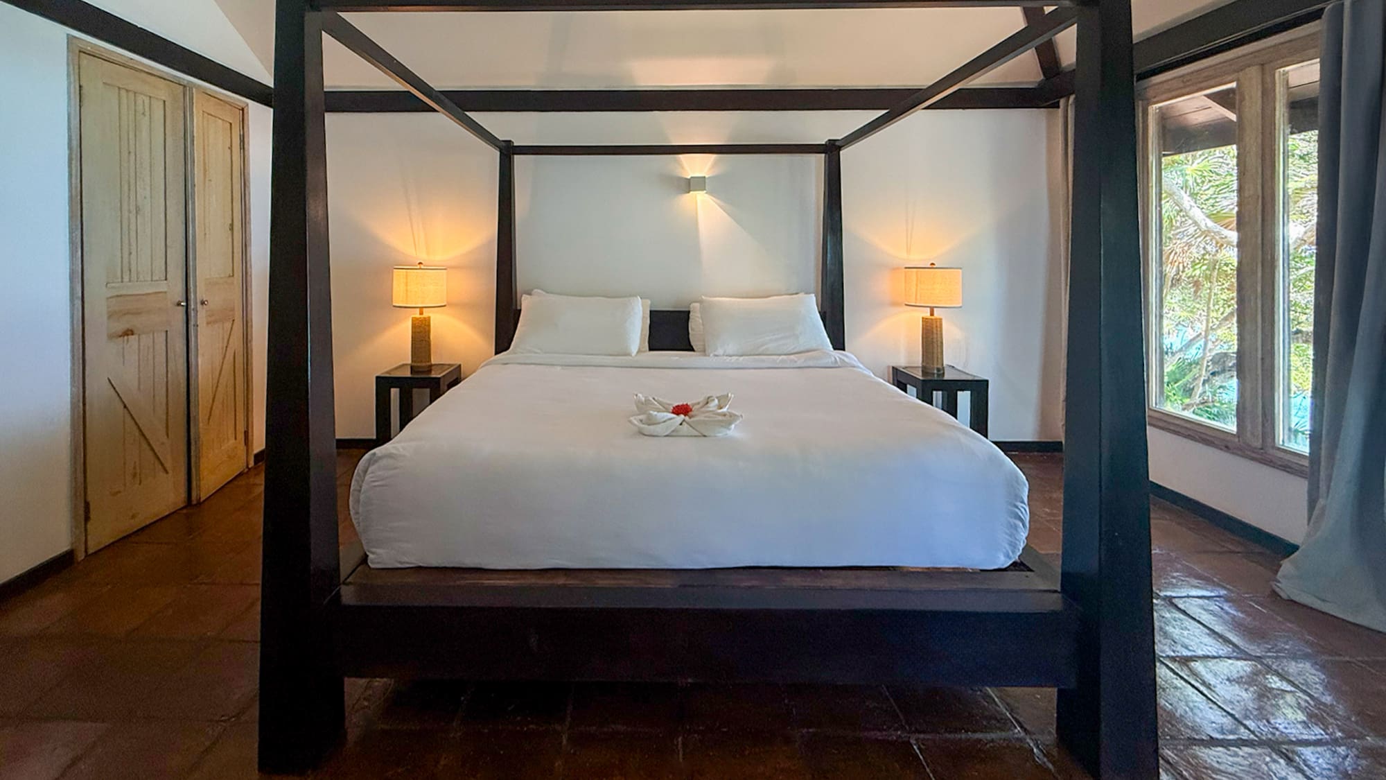 Tropical hotel bedroom with dark four-poster bed and terracotta floor.