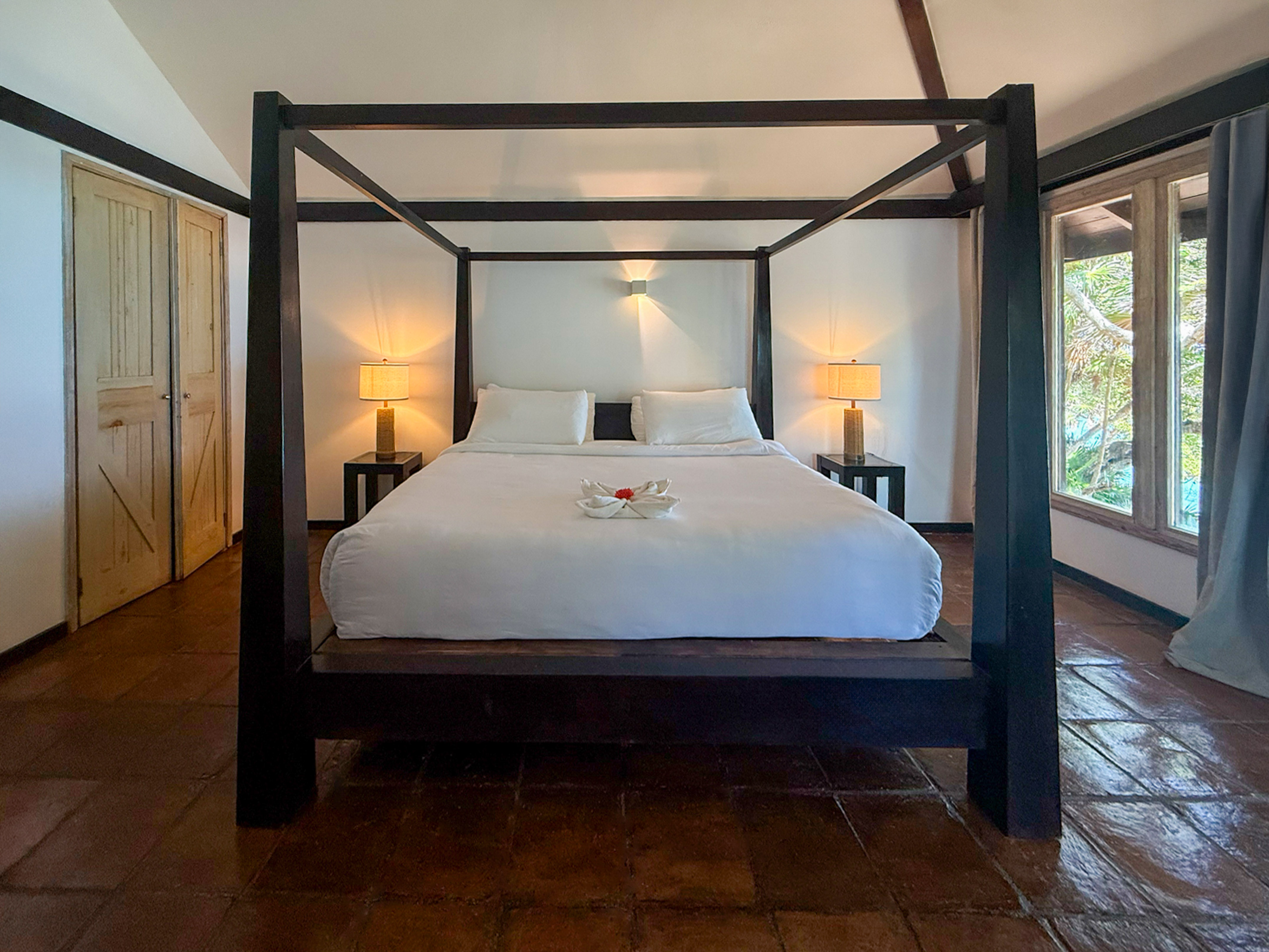 Tropical hotel bedroom with dark four-poster bed and terracotta floor.