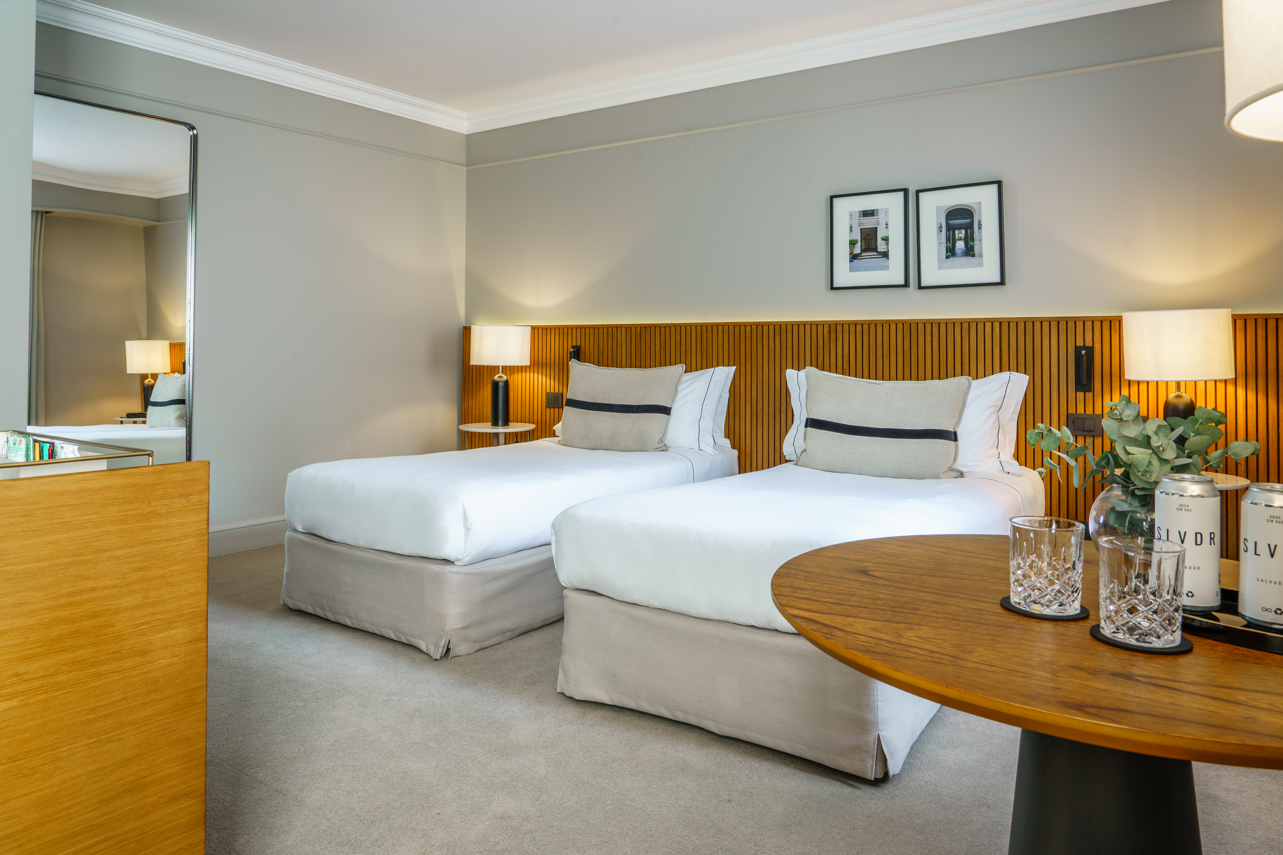 Modern hotel room with two twin beds, wooden headboard, and decorative table.