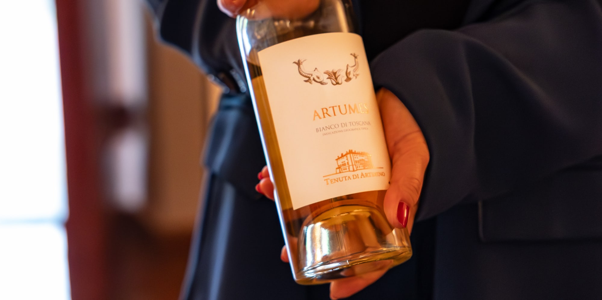 Artumes Bianco di Toscana white wine bottle held by hands.
