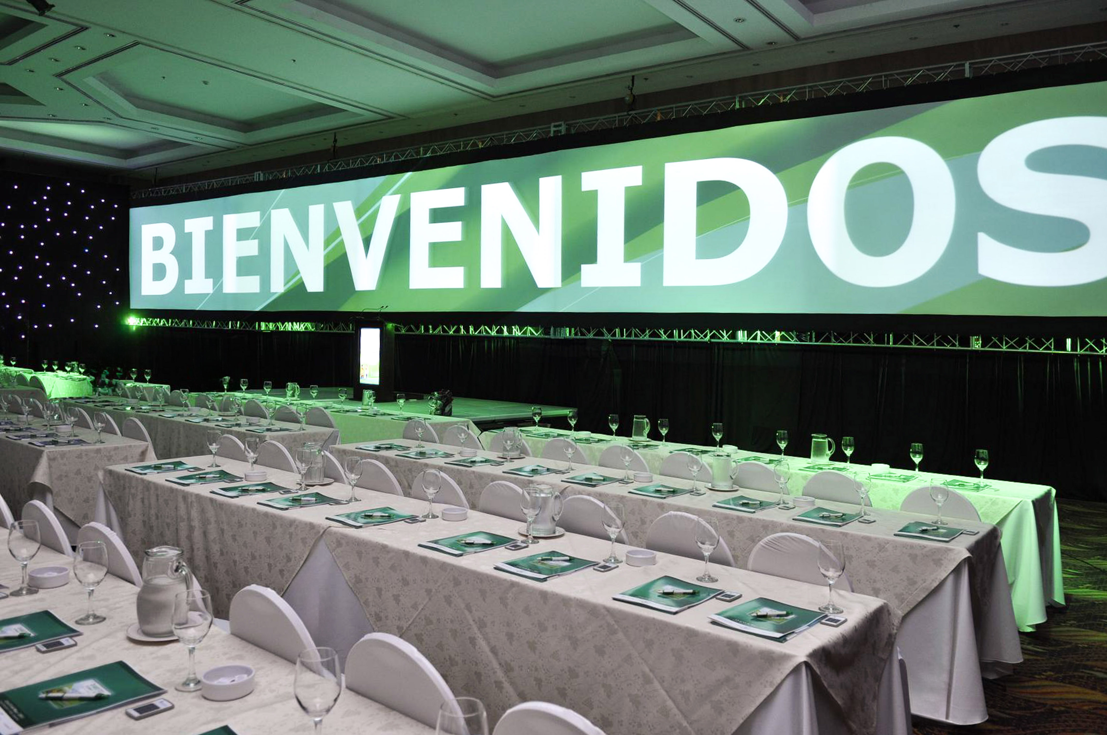 Conference room with "BIENVENIDOS" welcome screen and tables set for attendees.