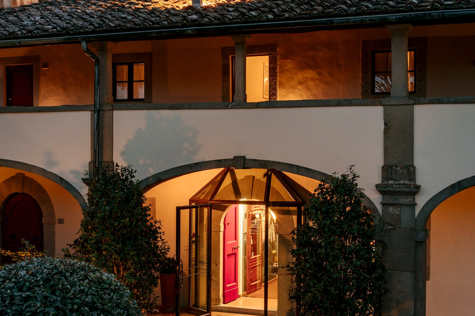 Tuscan villa evening entrance, warm lights, arched facade, lush garden.