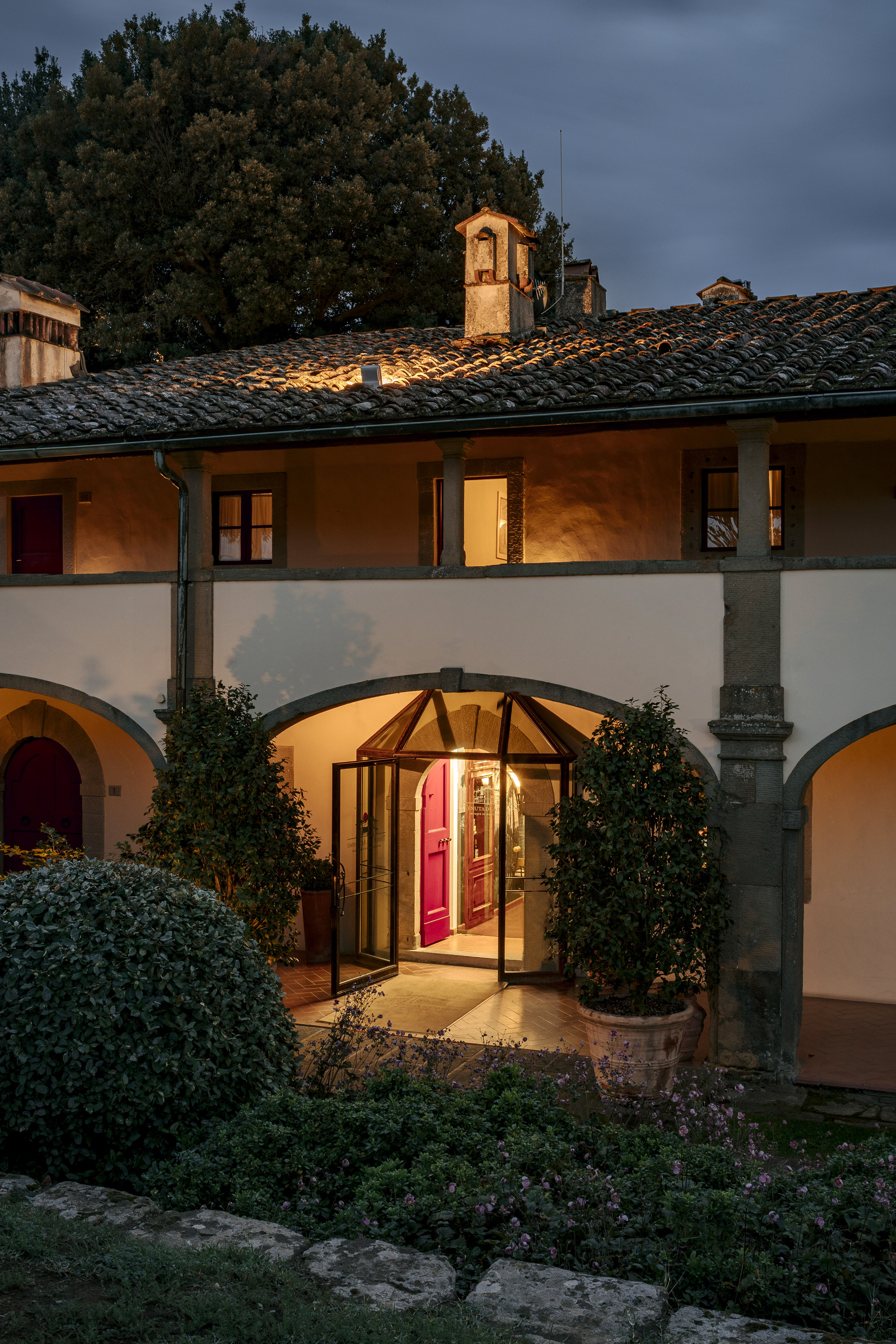 Tuscan villa evening entrance, warm lights, arched facade, lush garden.