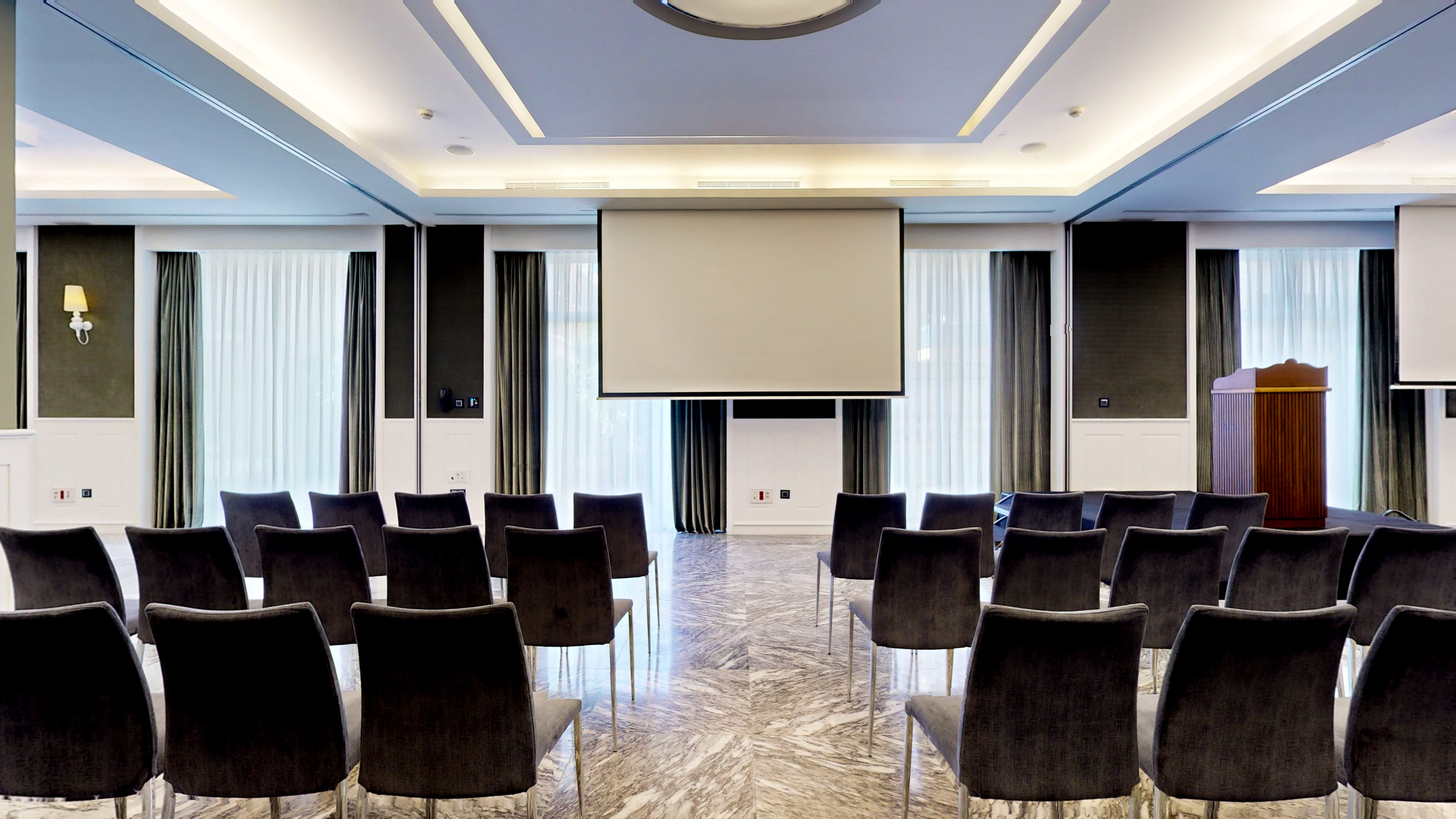Elegant meeting room with projector screen, podium, and dark chairs.