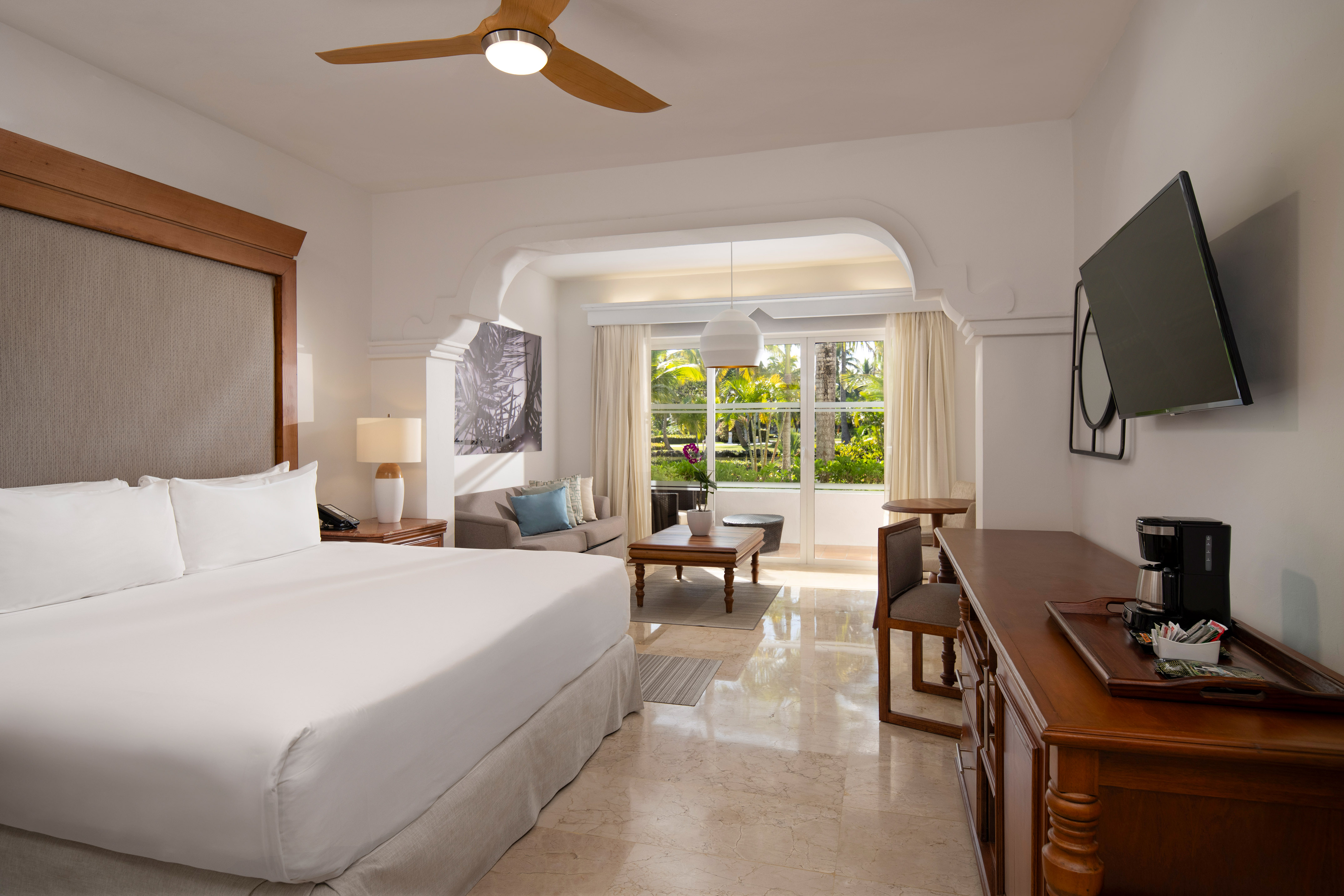 Spacious hotel suite with king bed, living area, and tropical garden view.