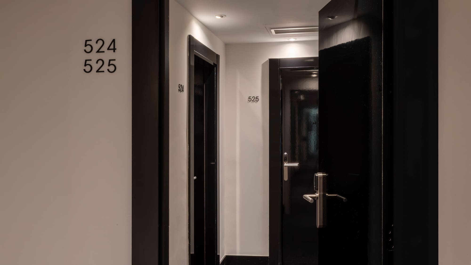 Modern hotel corridor with black doors, room numbers 524 and 525.