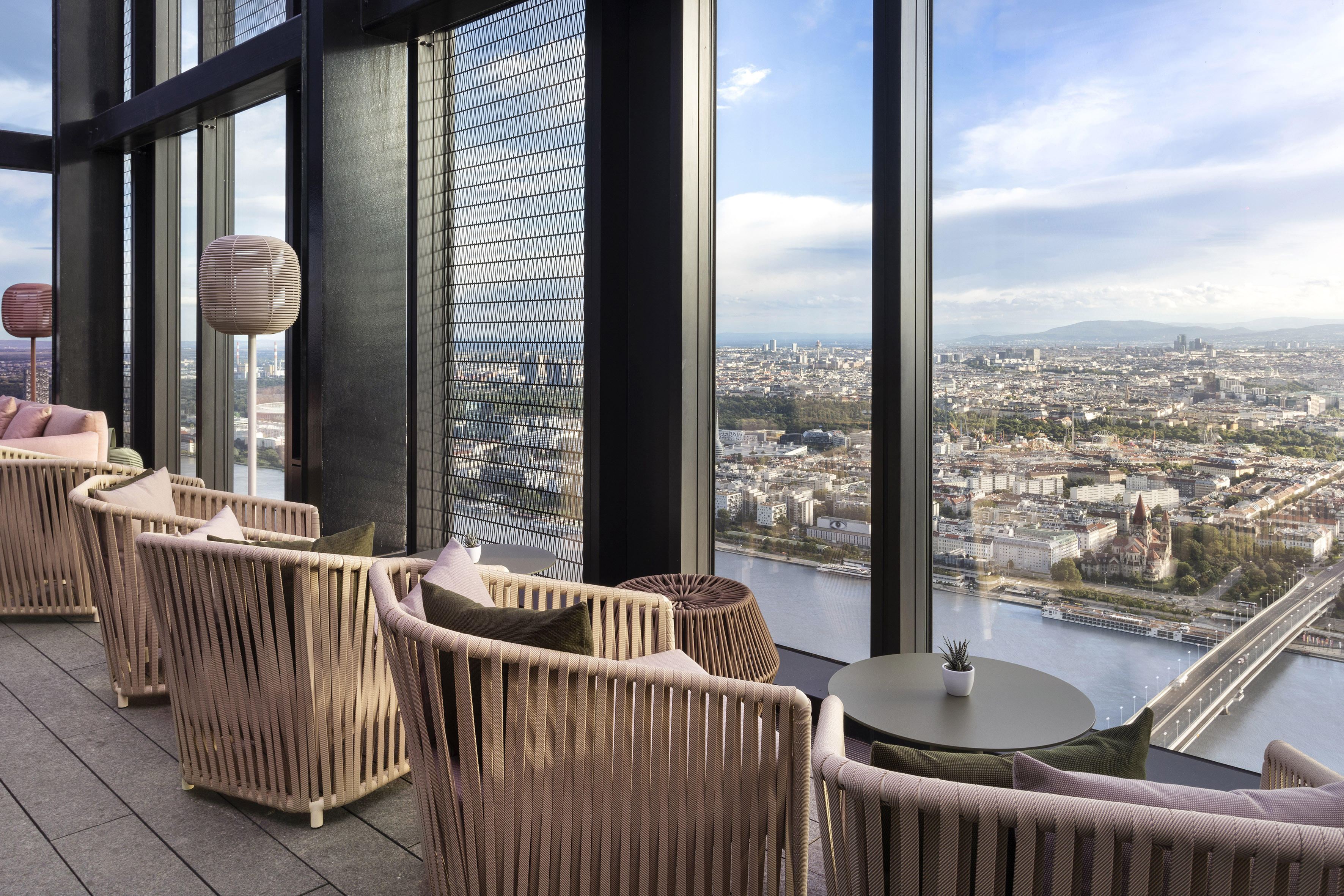 Modern high-rise lounge terrace with panoramic Vienna cityscape and river views.