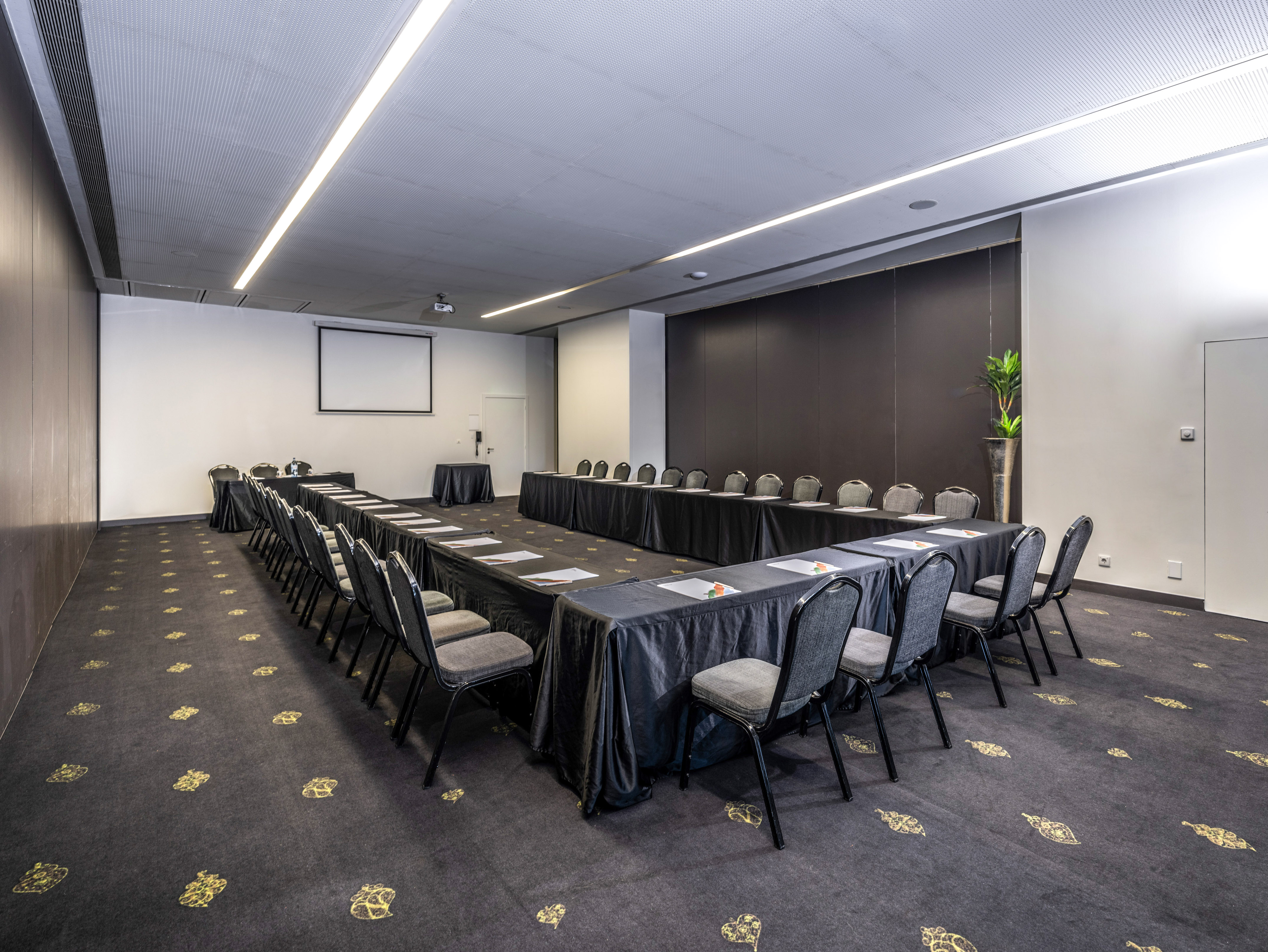 Modern U-shaped meeting room with projector screen and dark patterned carpet.