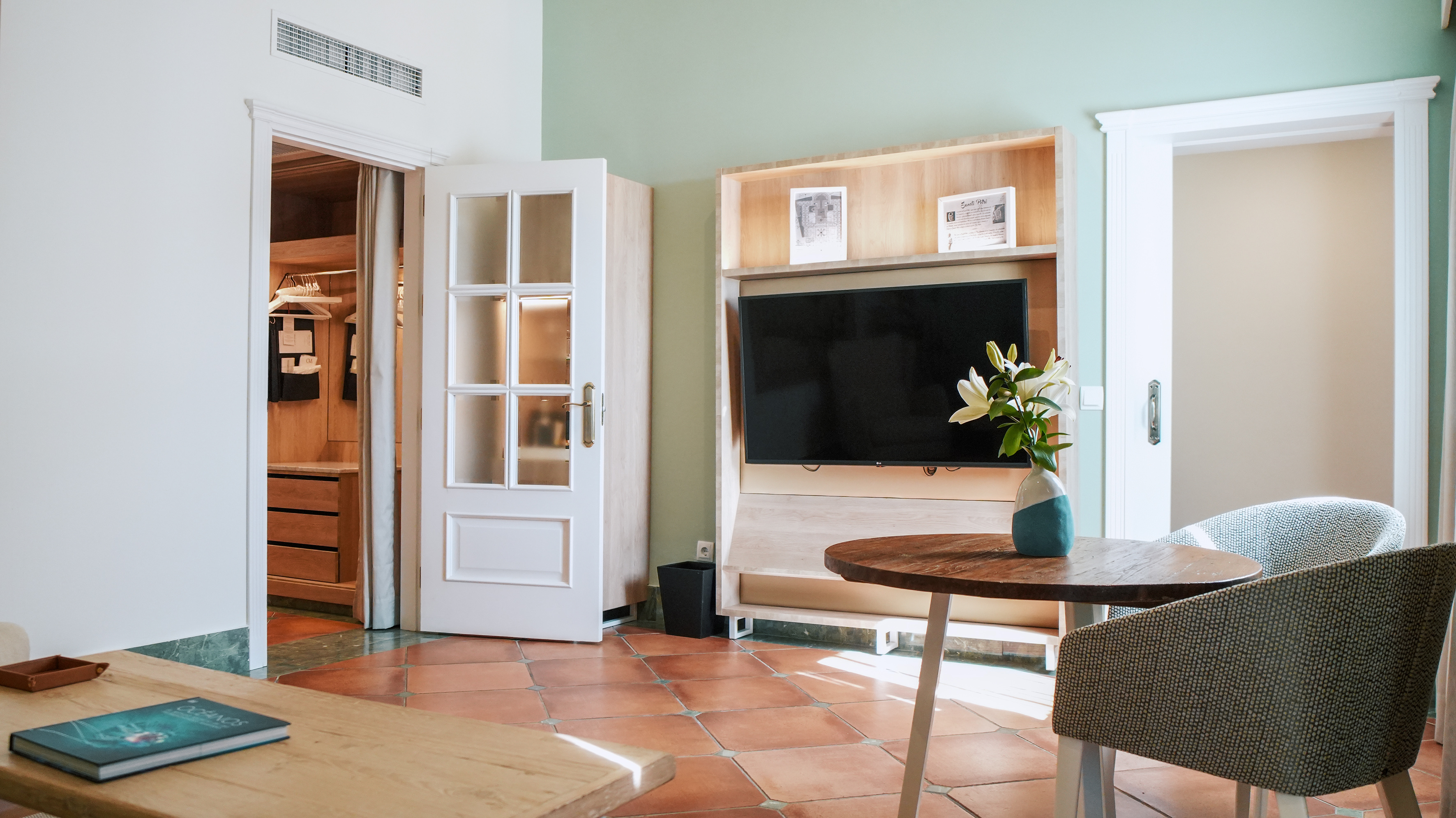 Hotel suite with terracotta floor, TV, open closet, and white lilies.