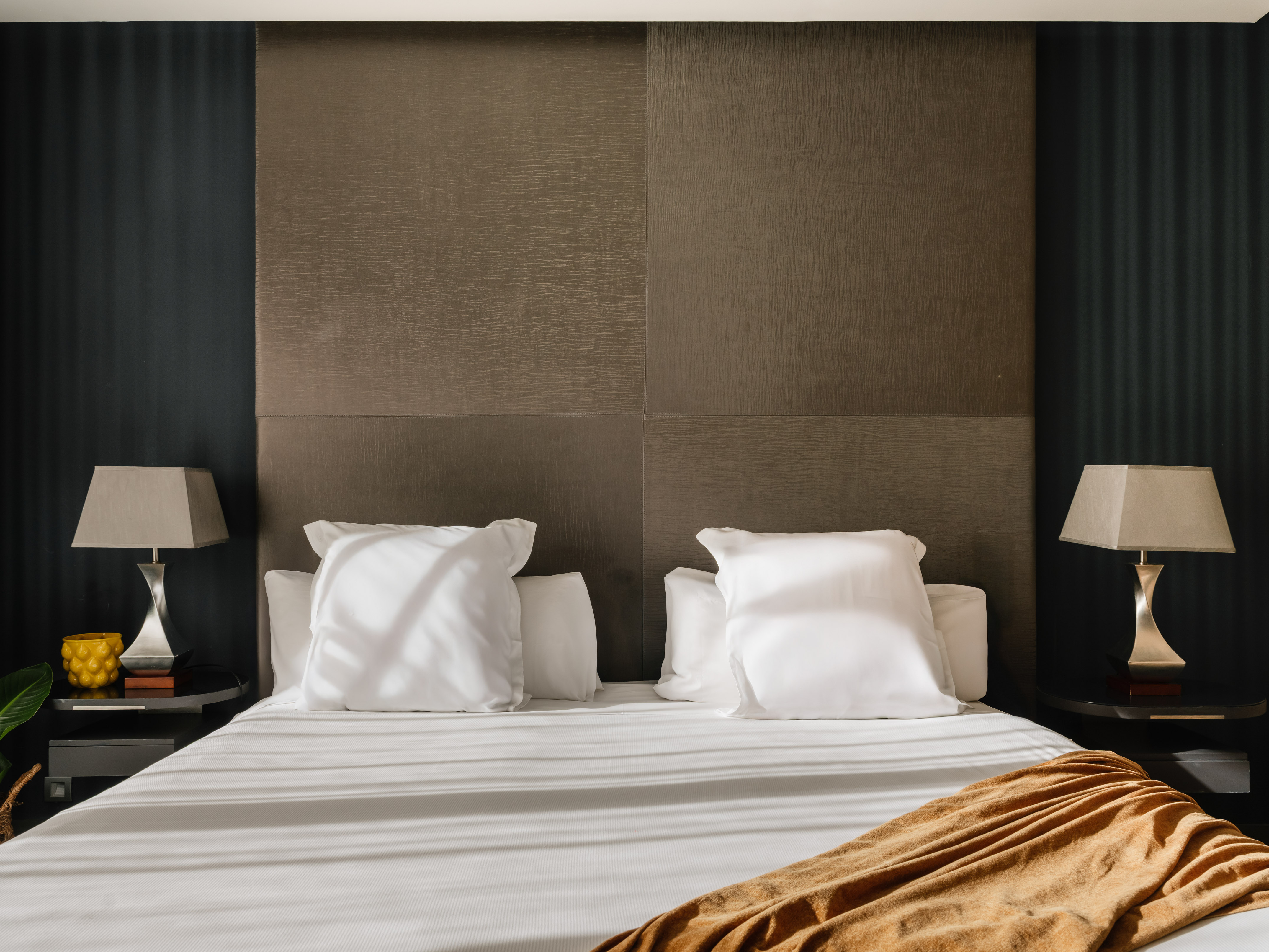 Modern bedroom with dark textured headboard, white bedding, and bedside lamps.
