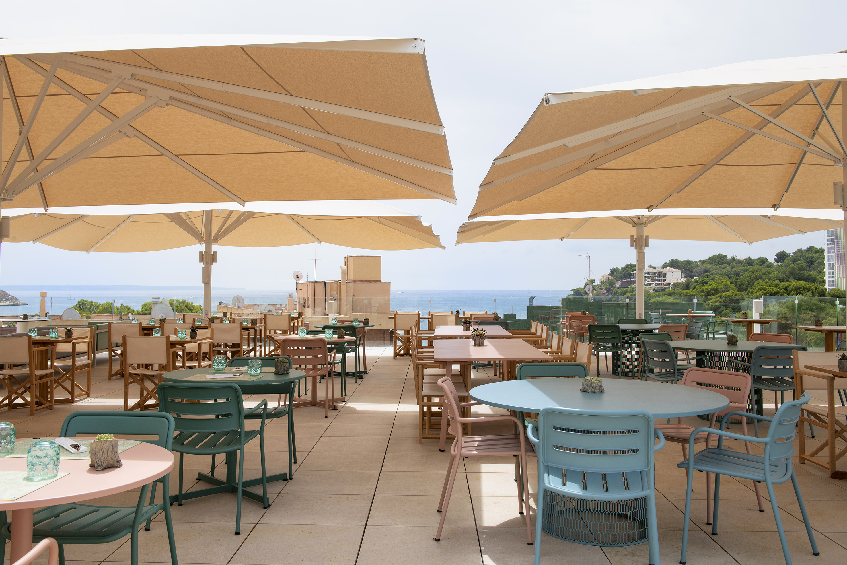 Rooftop restaurant terrace with colorful tables, chairs, large umbrellas, and sea view.