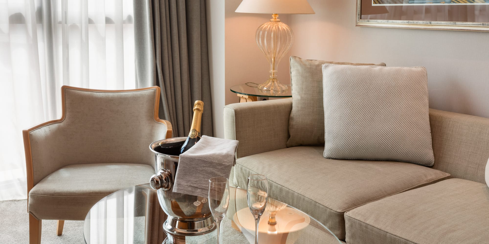 Hotel suite living area with champagne, flutes, sofa, and armchair.