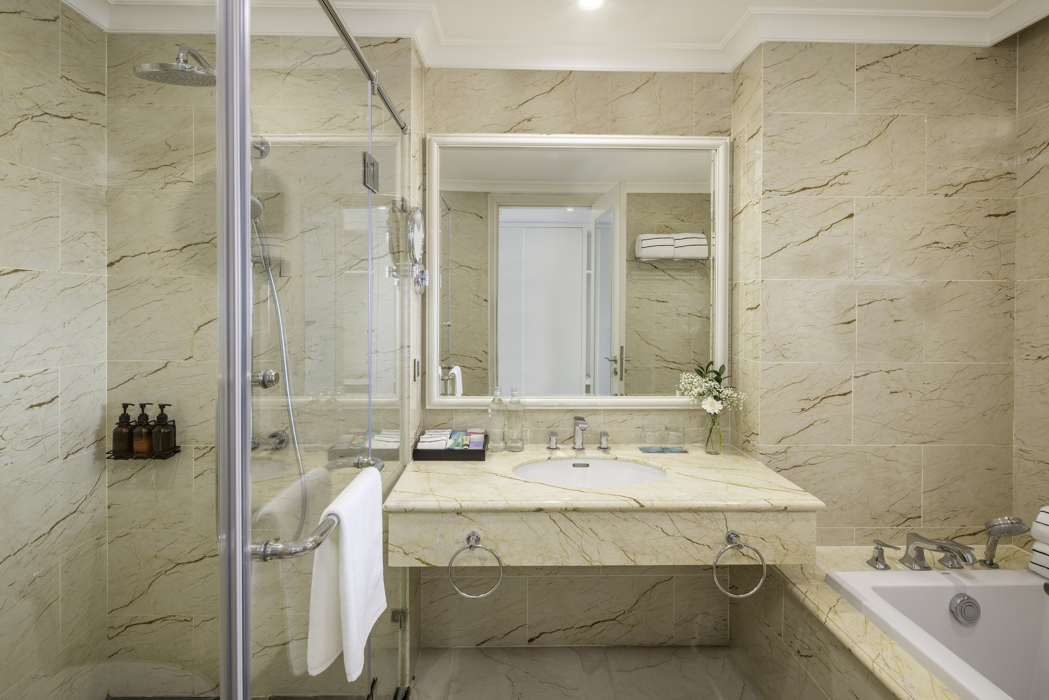 Luxurious marble hotel bathroom with glass shower, vanity, and bathtub.