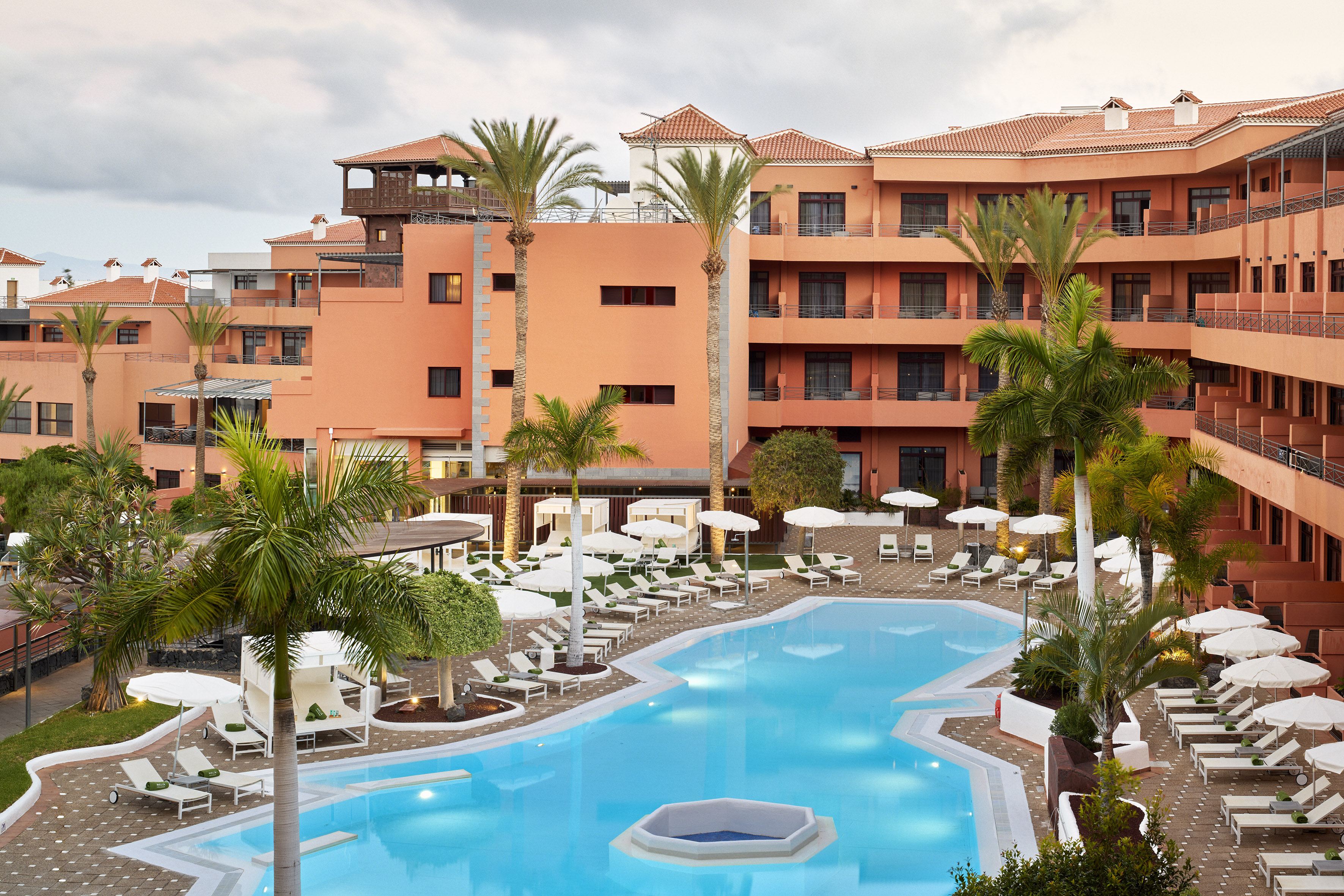 Terracotta resort hotel, large swimming pool, palm trees, and lounge area.