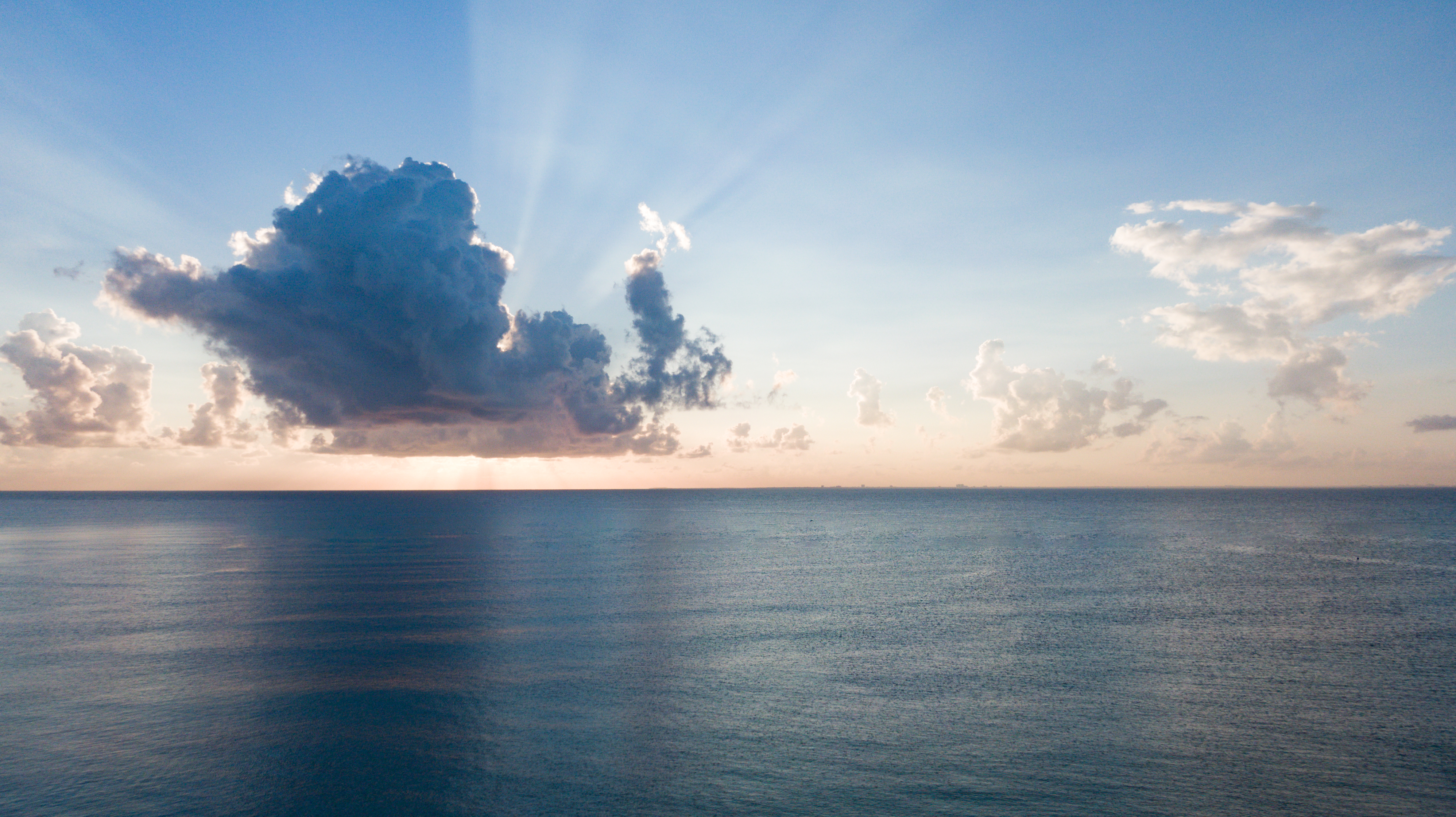 Calm ocean with sun rays piercing through dramatic clouds at sunrise.