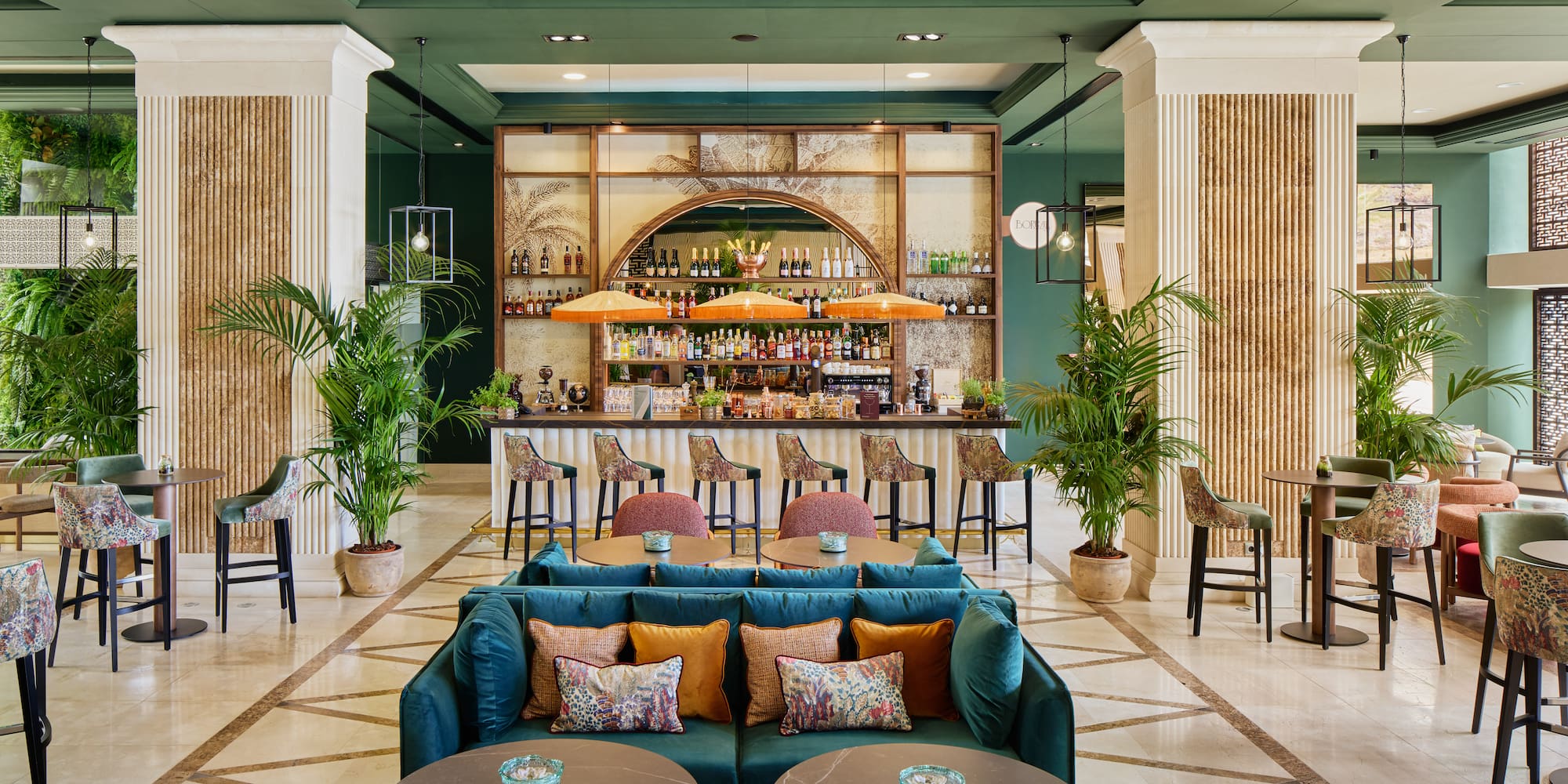 Luxurious hotel lobby bar with tropical decor, green walls, and plush seating.