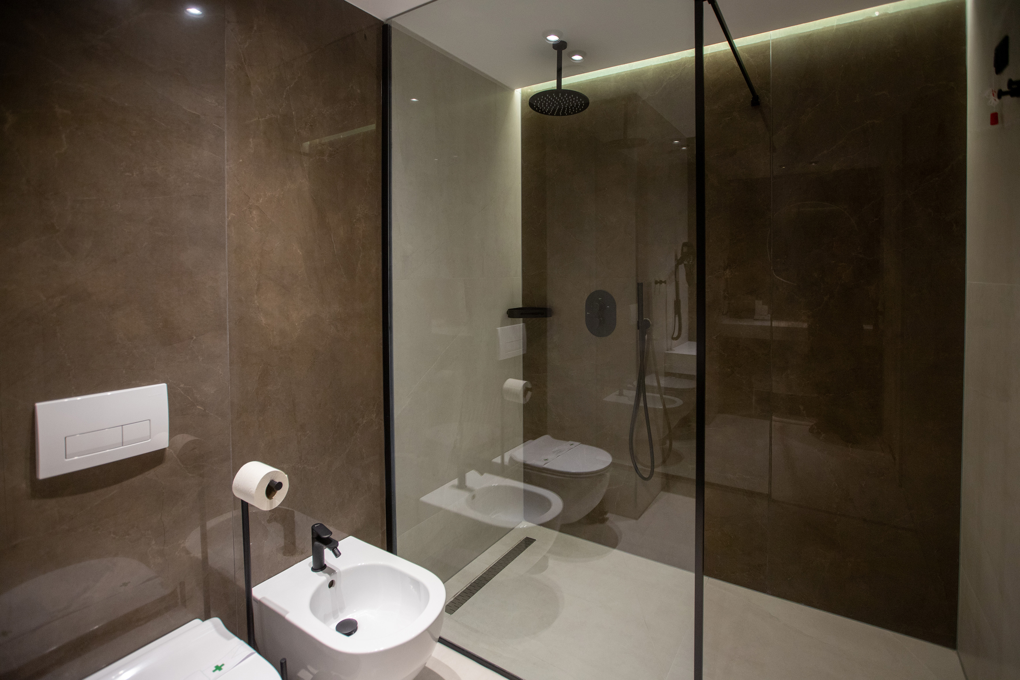 Modern bathroom with glass shower, wall toilet, bidet, and luxurious marble walls.