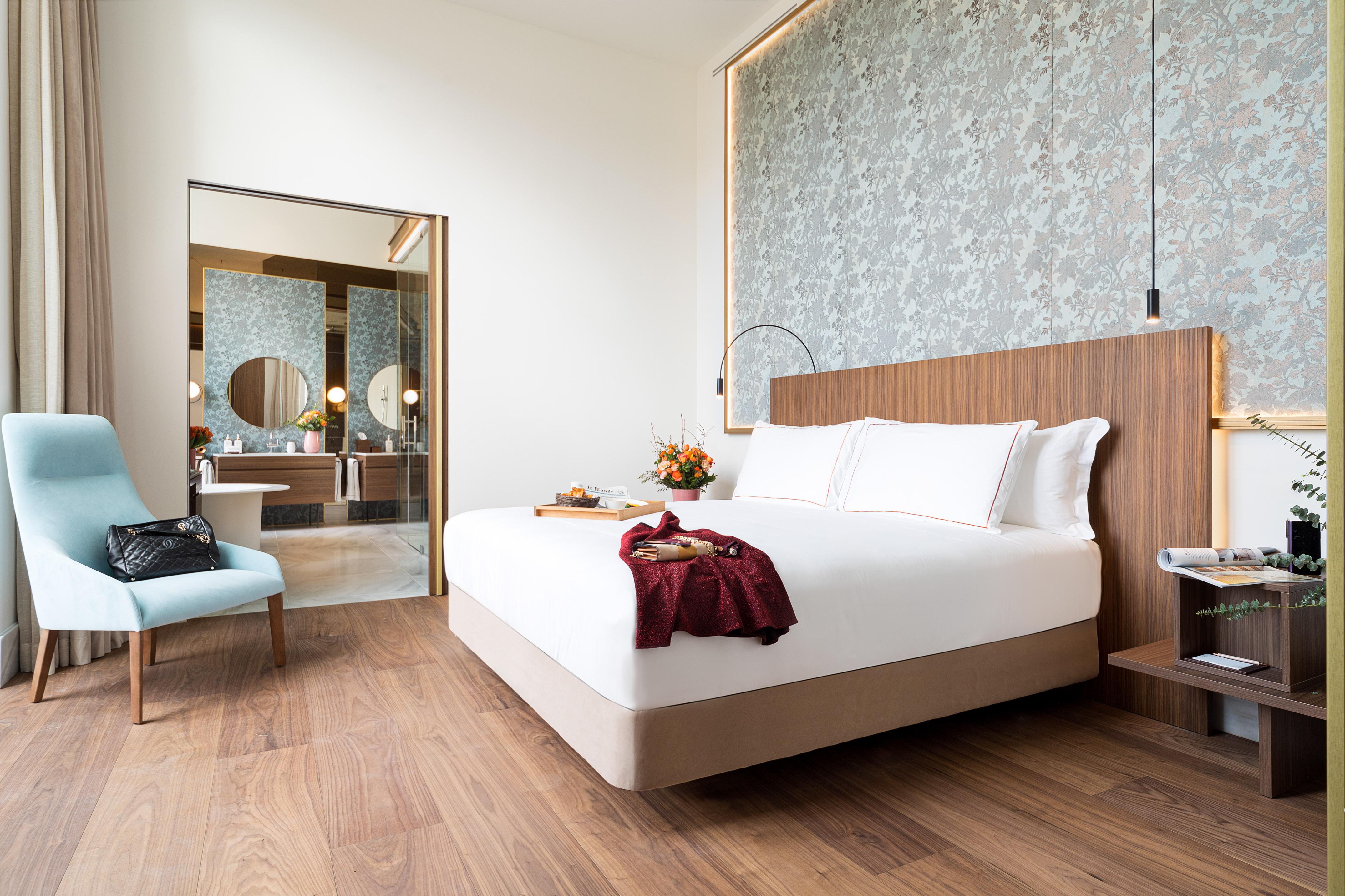 Modern luxury hotel room with king bed, wood floor, and open bathroom.