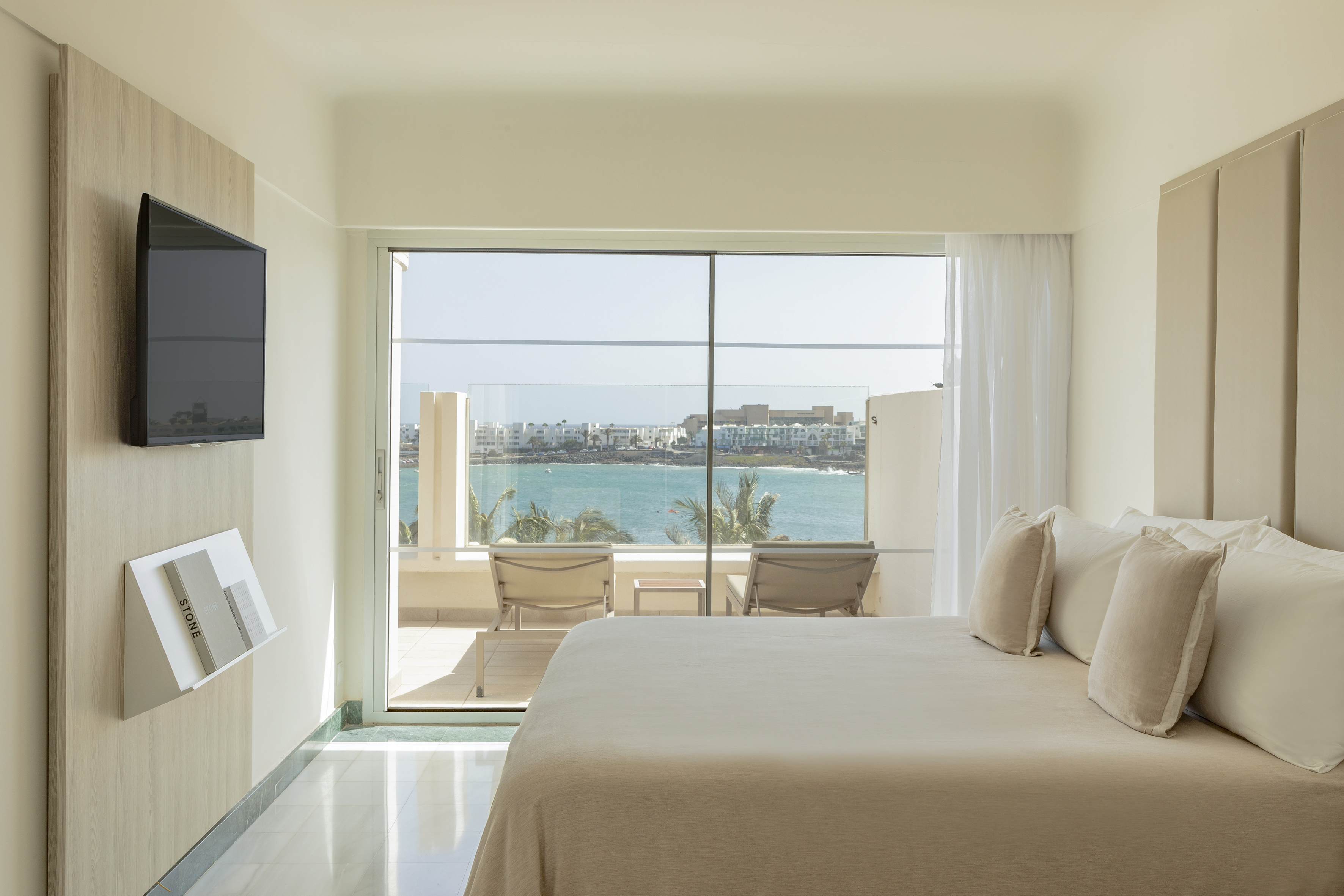 Modern hotel bedroom with ocean view balcony and comfortable bed.