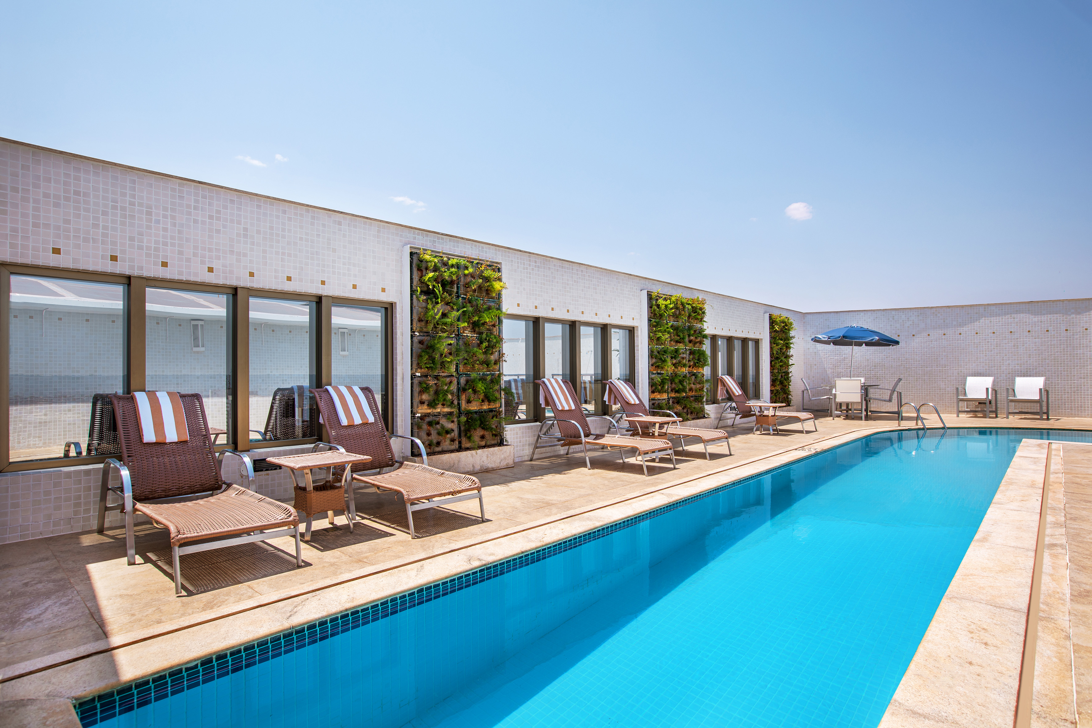 Hotel rooftop pool with sun loungers, vertical gardens.