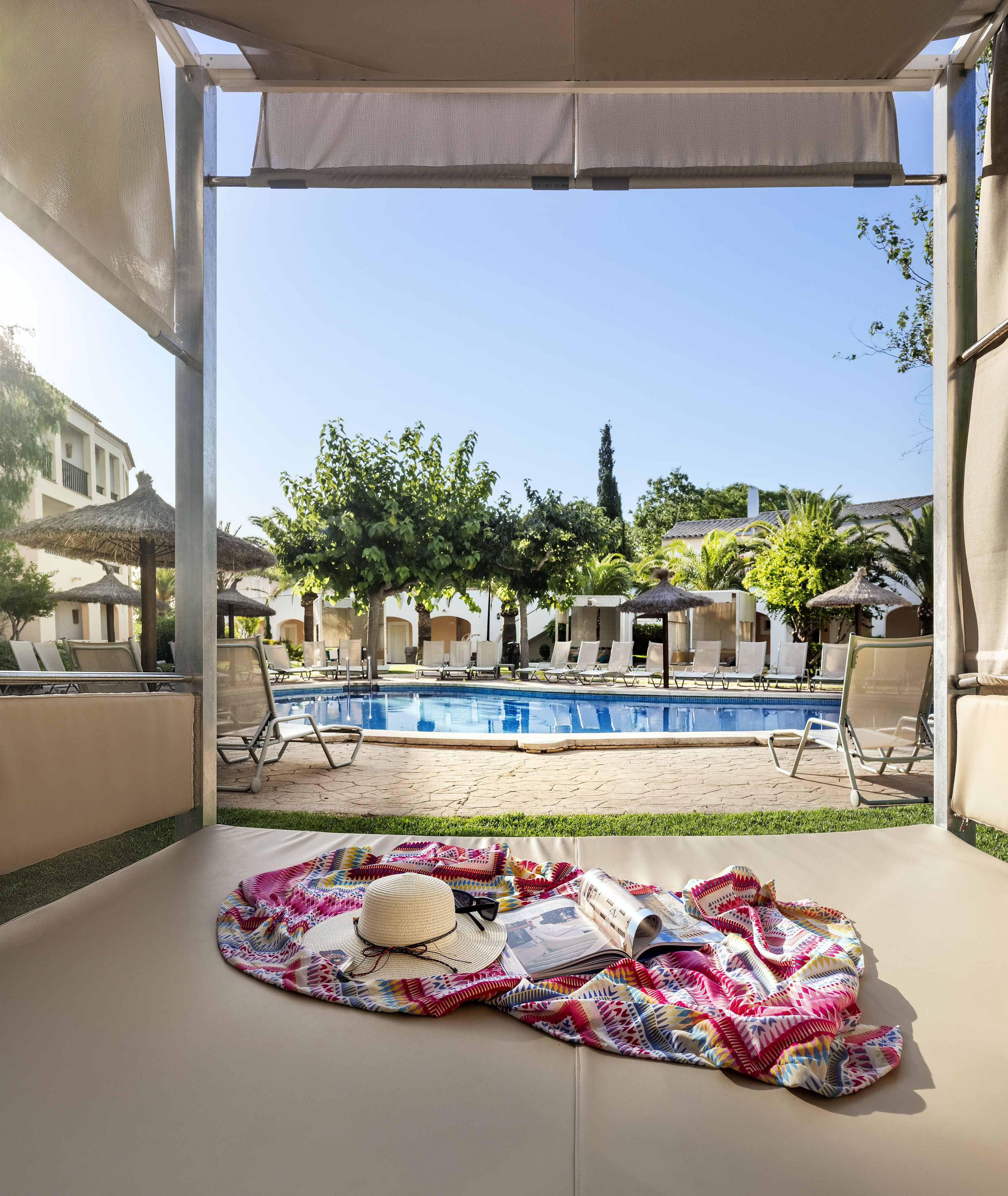 Resort pool view from cabana daybed with sunhat, magazine, colorful blanket. - XTRA SOL Suite - SOL Falcó Menorca, Menorca