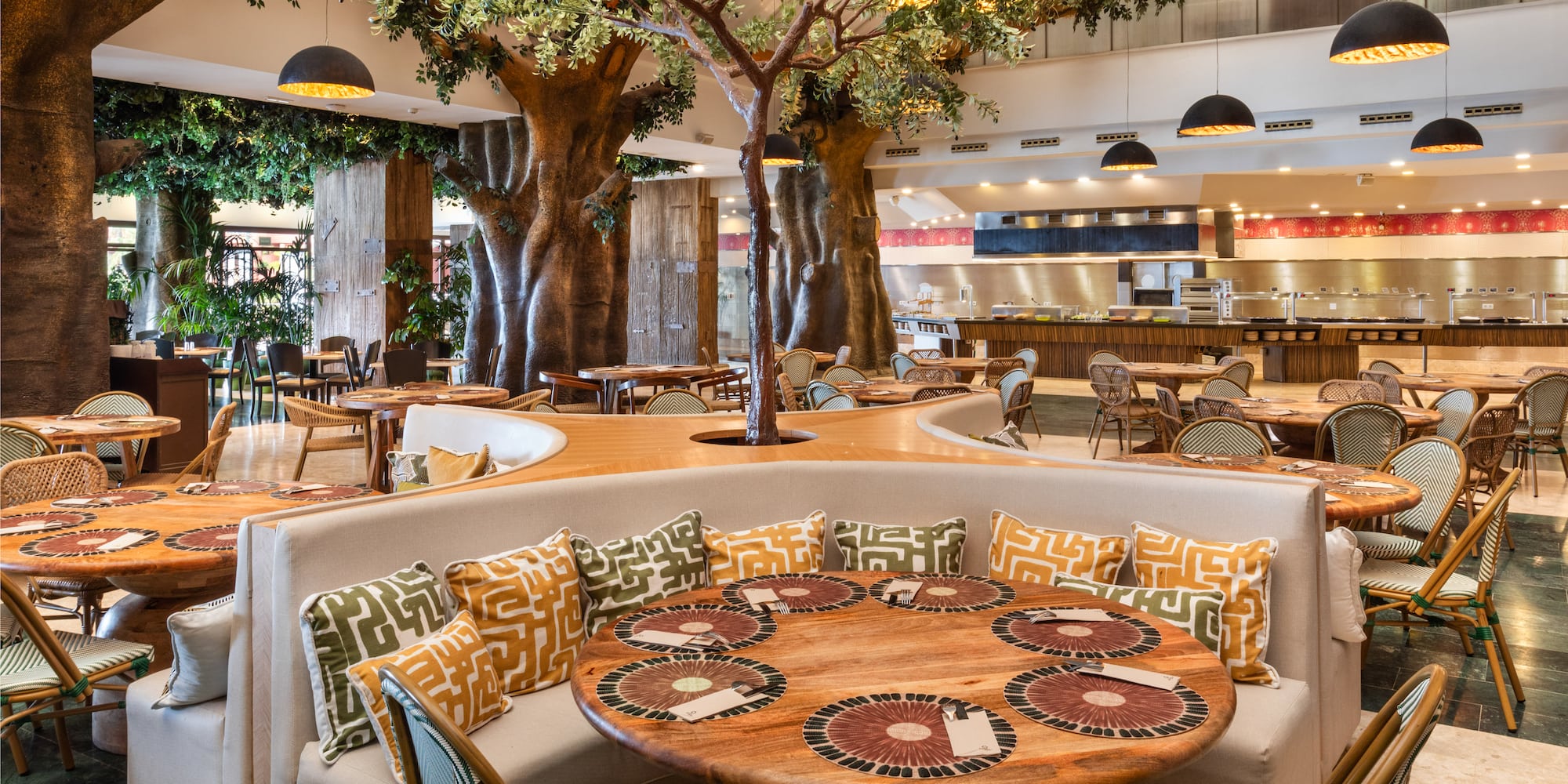Indoor restaurant with large tree decor, buffet, wooden tables, and booth seating.