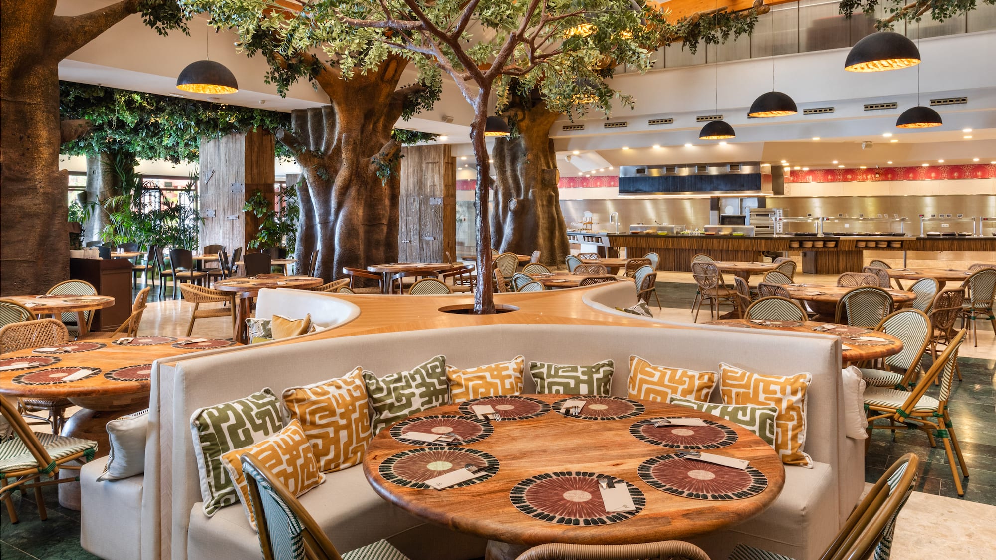 Spacious resort buffet restaurant with tree decor and dining tables.