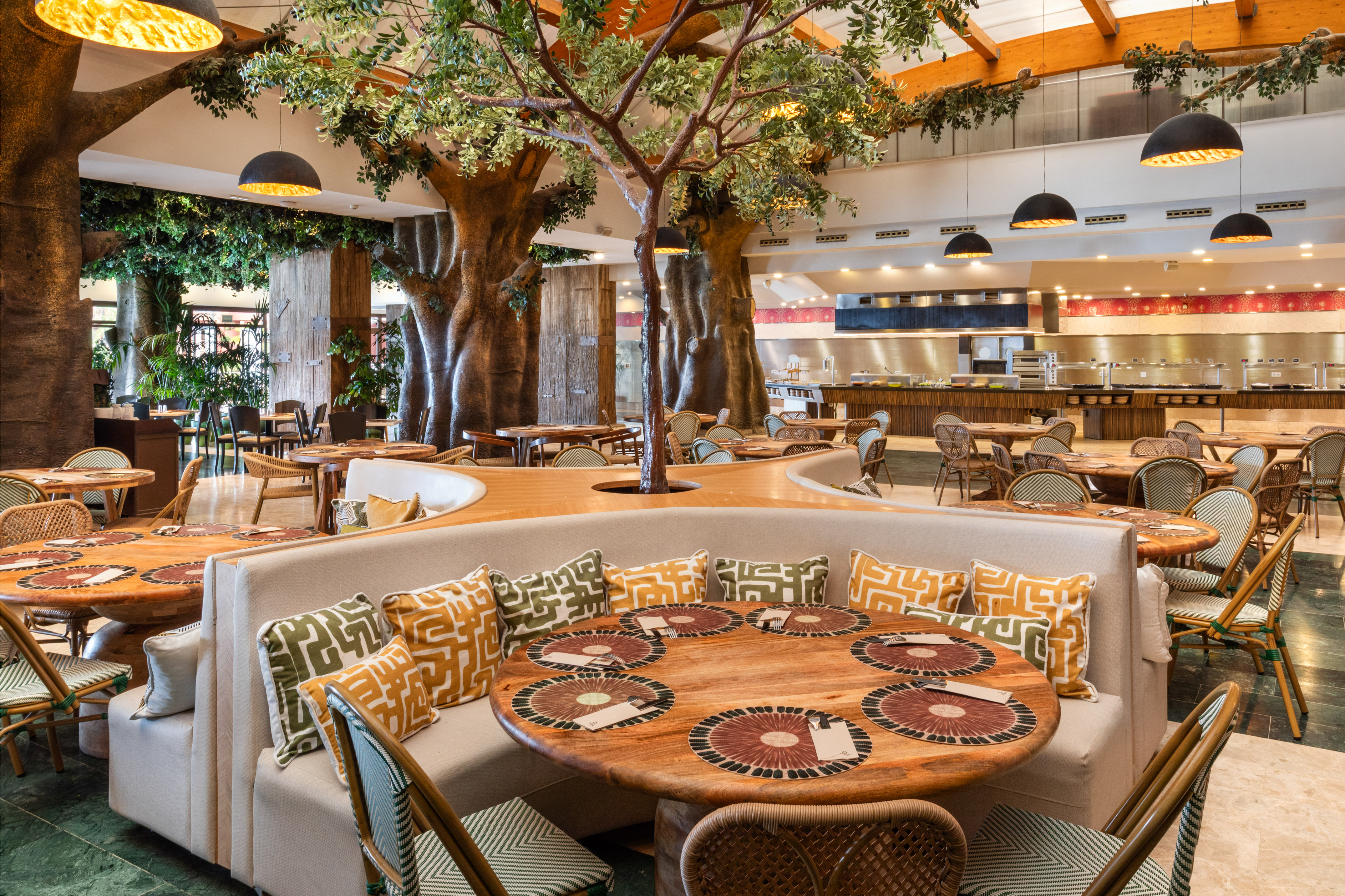 Indoor restaurant with large tree decor, buffet, wooden tables, and booth seating.
