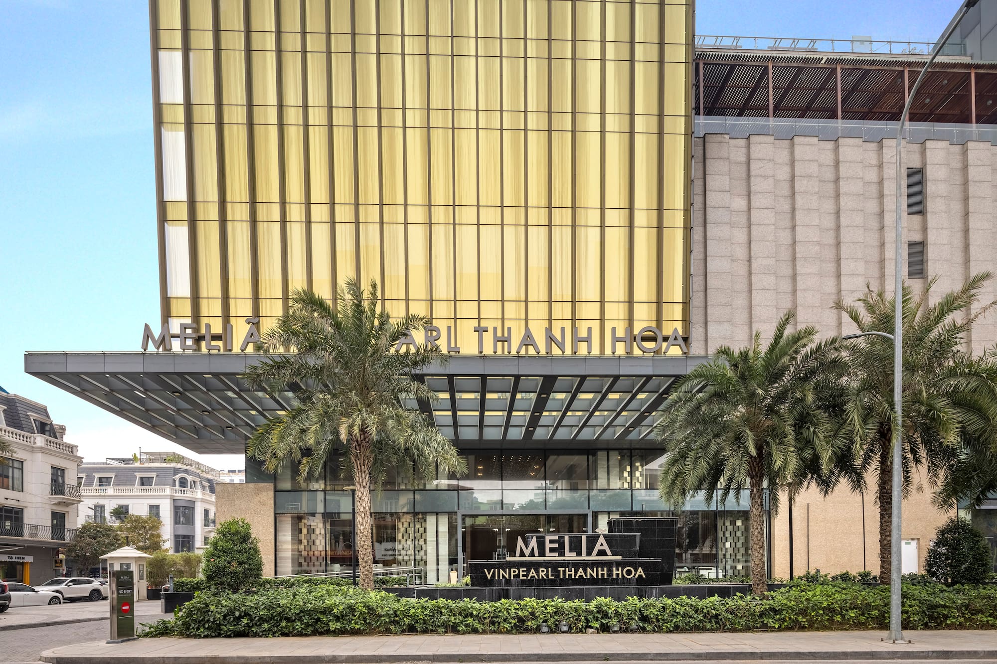 Modern Melia Vinpearl Thanh Hoa hotel with gold facade and palm trees.