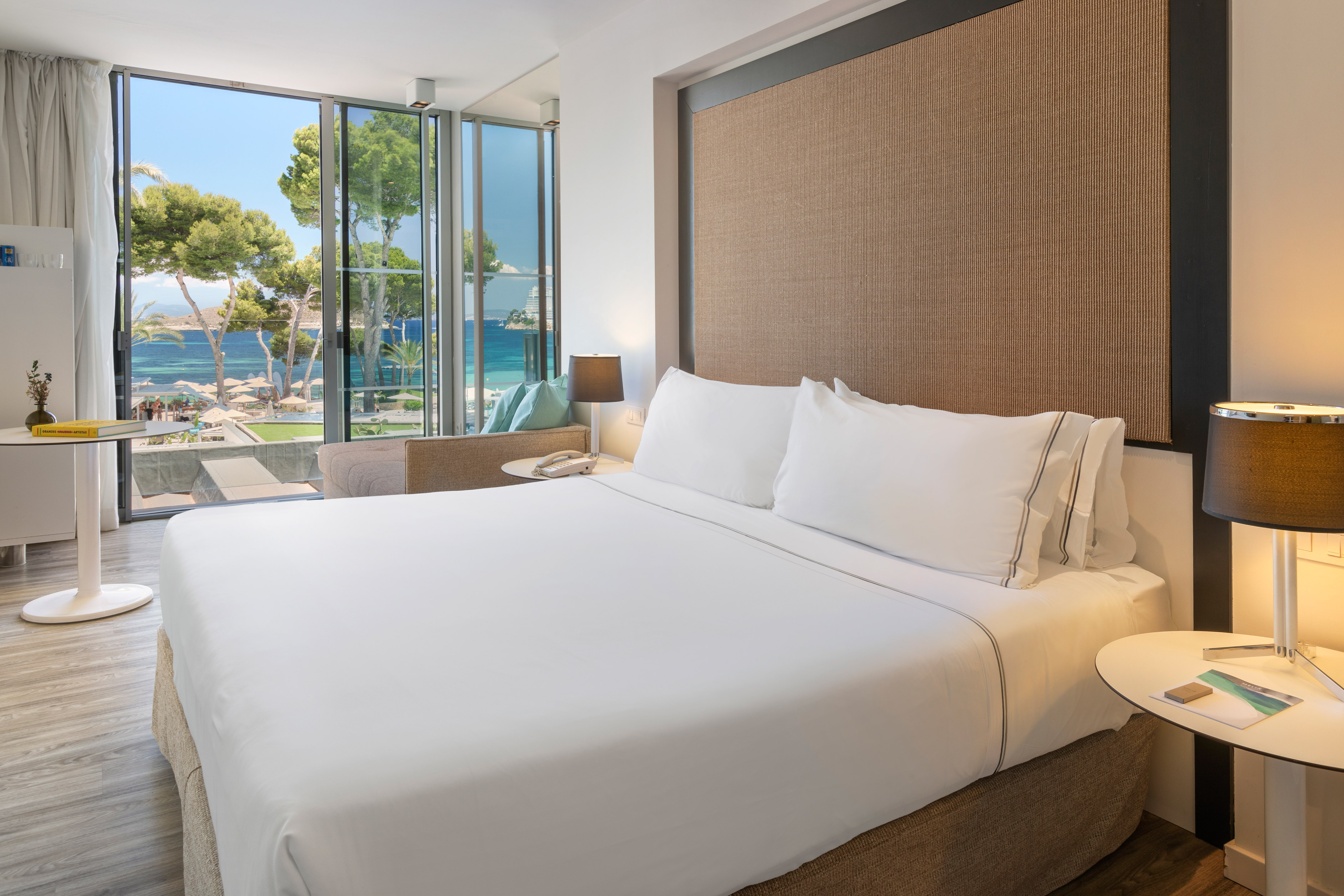 Modern hotel room with ocean view, large bed, and beach through glass doors.