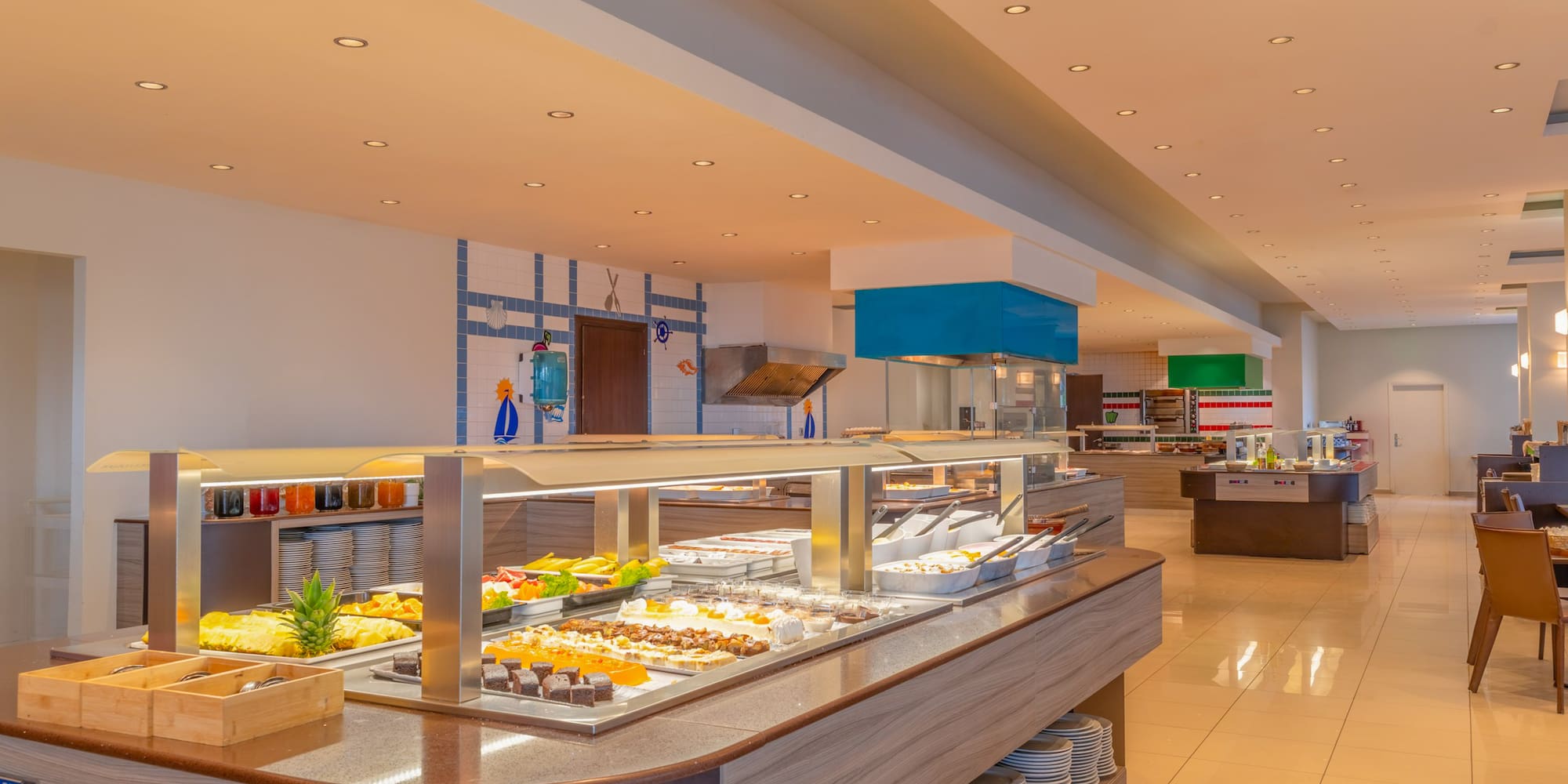 Bright hotel dining buffet featuring fresh food, fruits, and varied desserts.